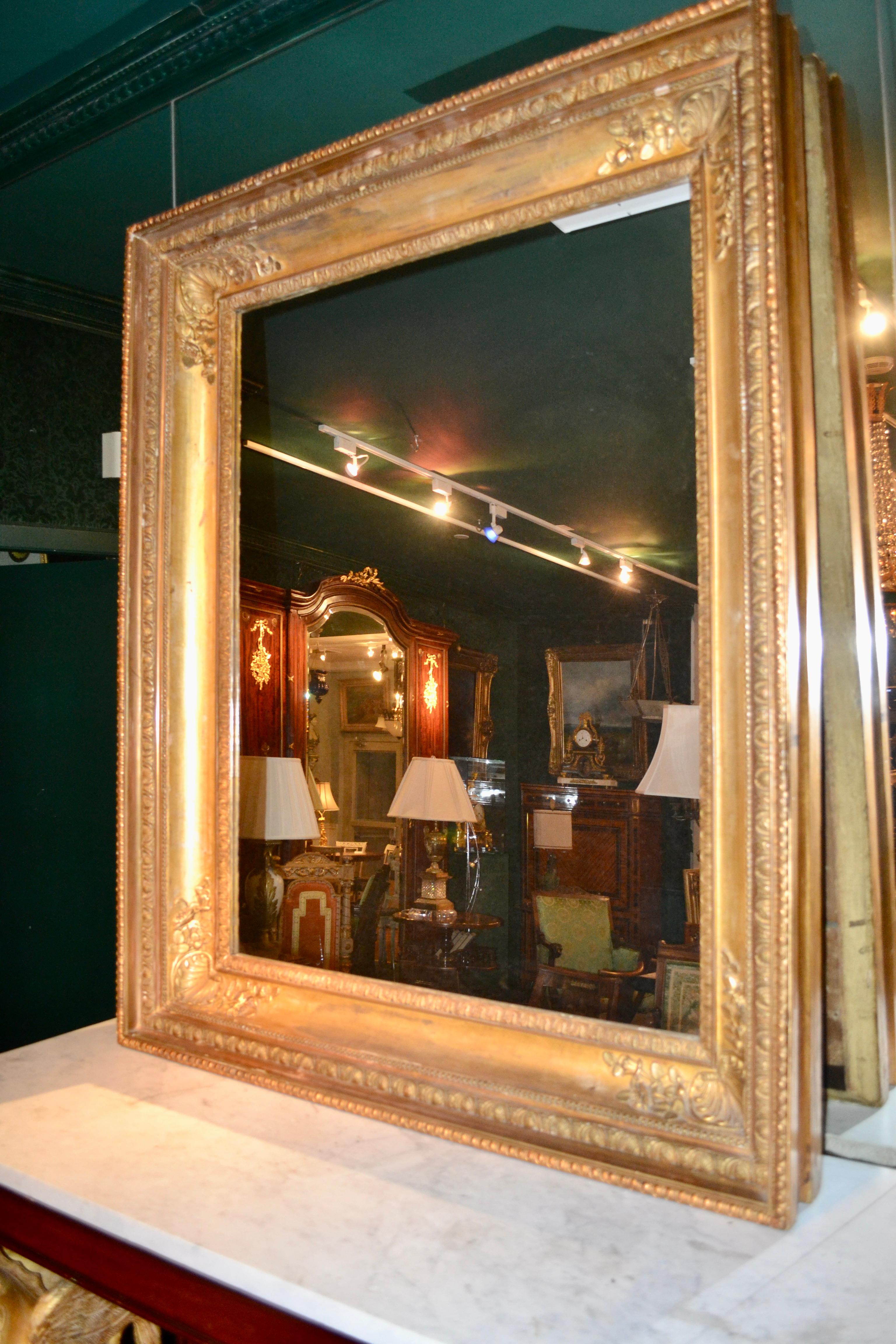 A large French Empire  carved and original water gilded Empire picture frame inset with a modern mirror, the corners of the deeply scooped sides set with palmettes.
         