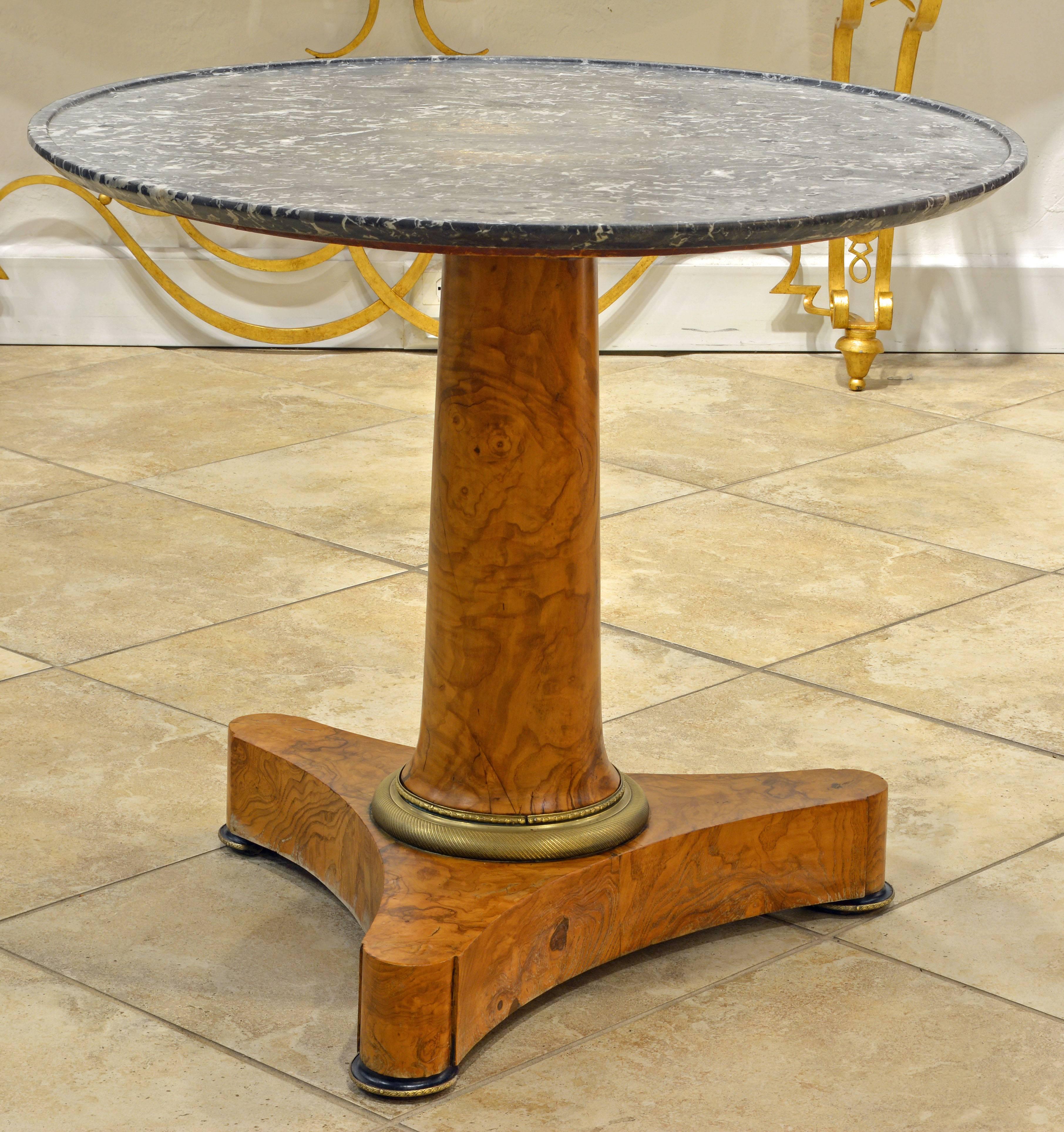 An iconic and distinguished design characterizes this table featuring a black/gray/white dish-carved marble top supported by a single conical stem and gilt bronze foot resting on a three pointed base with gilt bronze and ebonized feet.