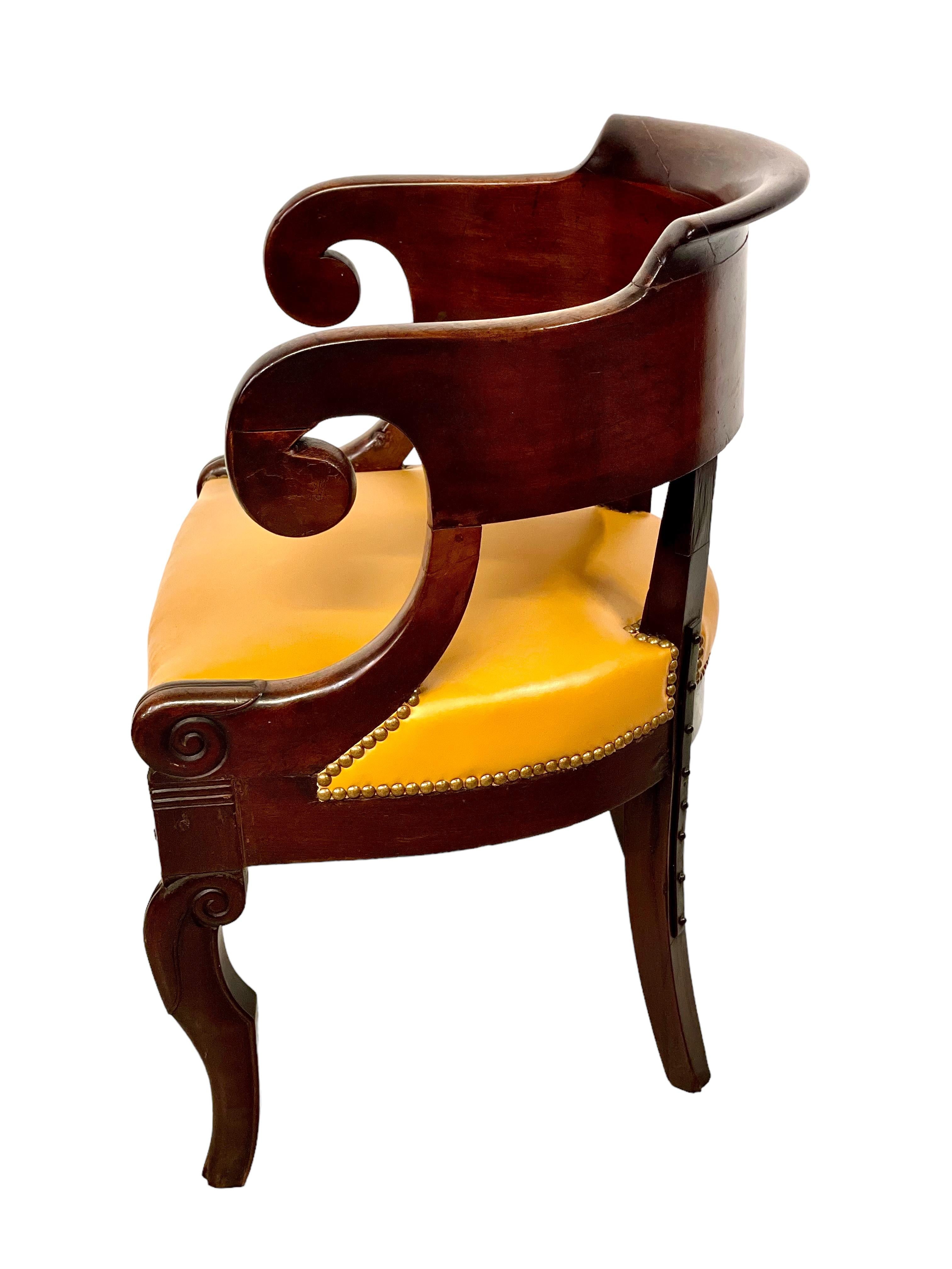 A handsome and well-proportioned French Empire period office chair, featuring a wonderfully curved gondola backrest and comfortable, padded golden leather upholstered seat, secured all round with nailhead trim. The carved and shaped front legs and