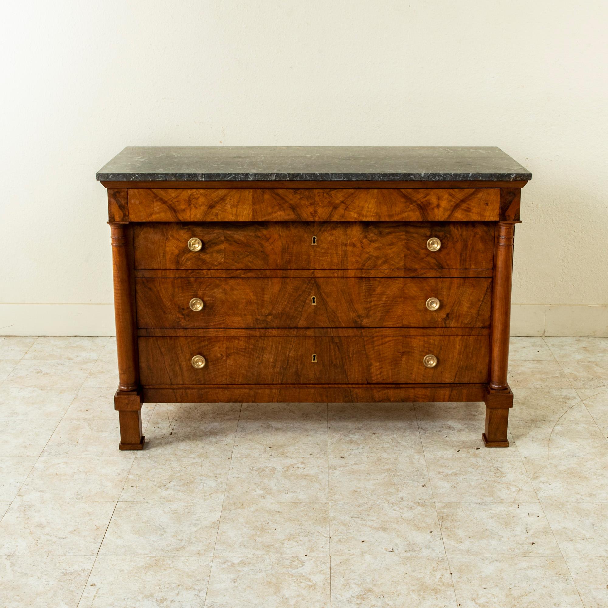 This early nineteenth century French Empire period book matched burl walnut commode or chest of drawers features a solid Saint Anne marble top and two detached columns resting on square plinths. Three drawers of dovetail construction are fitted with