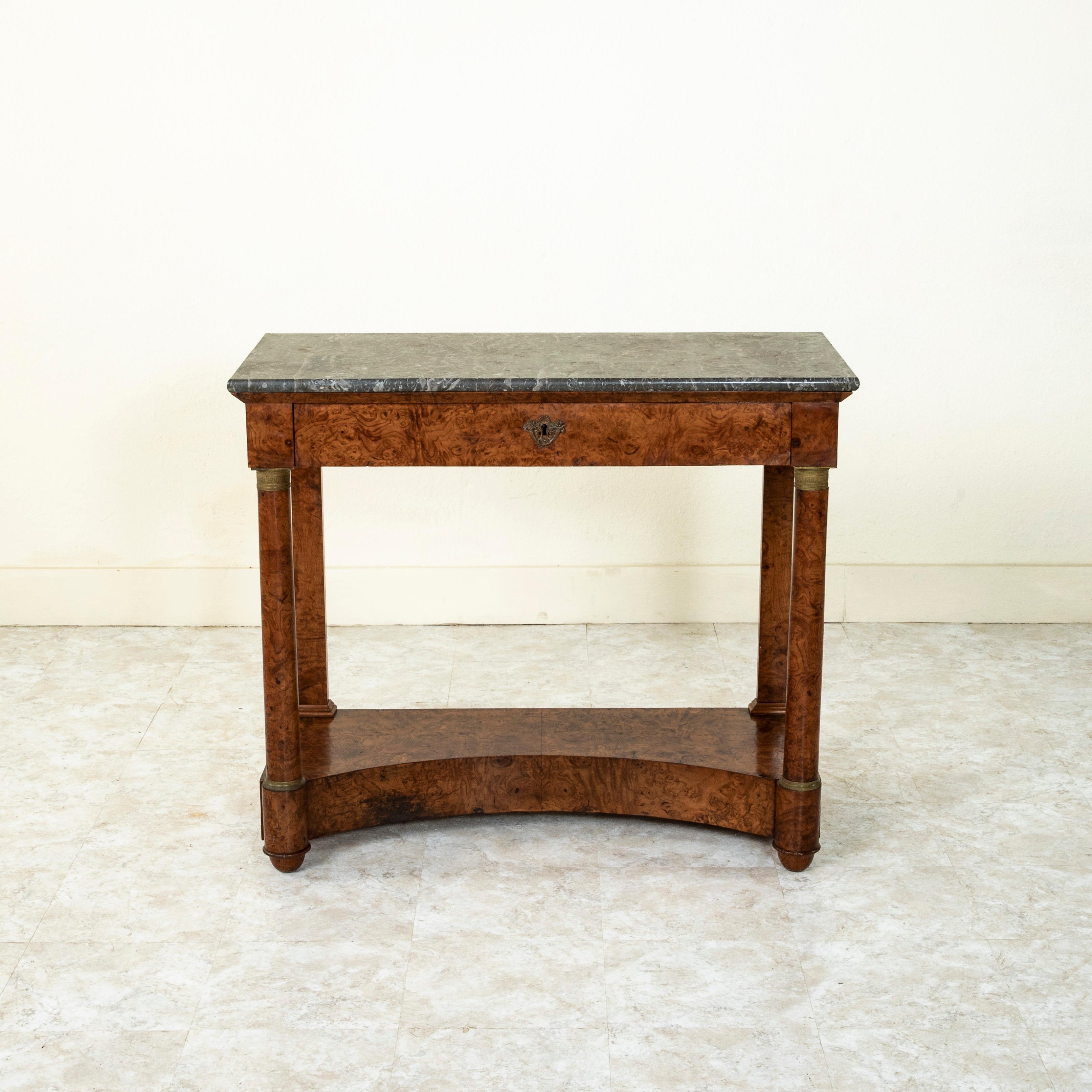 This early nineteenth century French Empire period burl walnut console table features columns at the front corners and a Saint Anne marble top. The columns are detailed with bronze capitals and bases detailed with spiral beading and palmettes. A