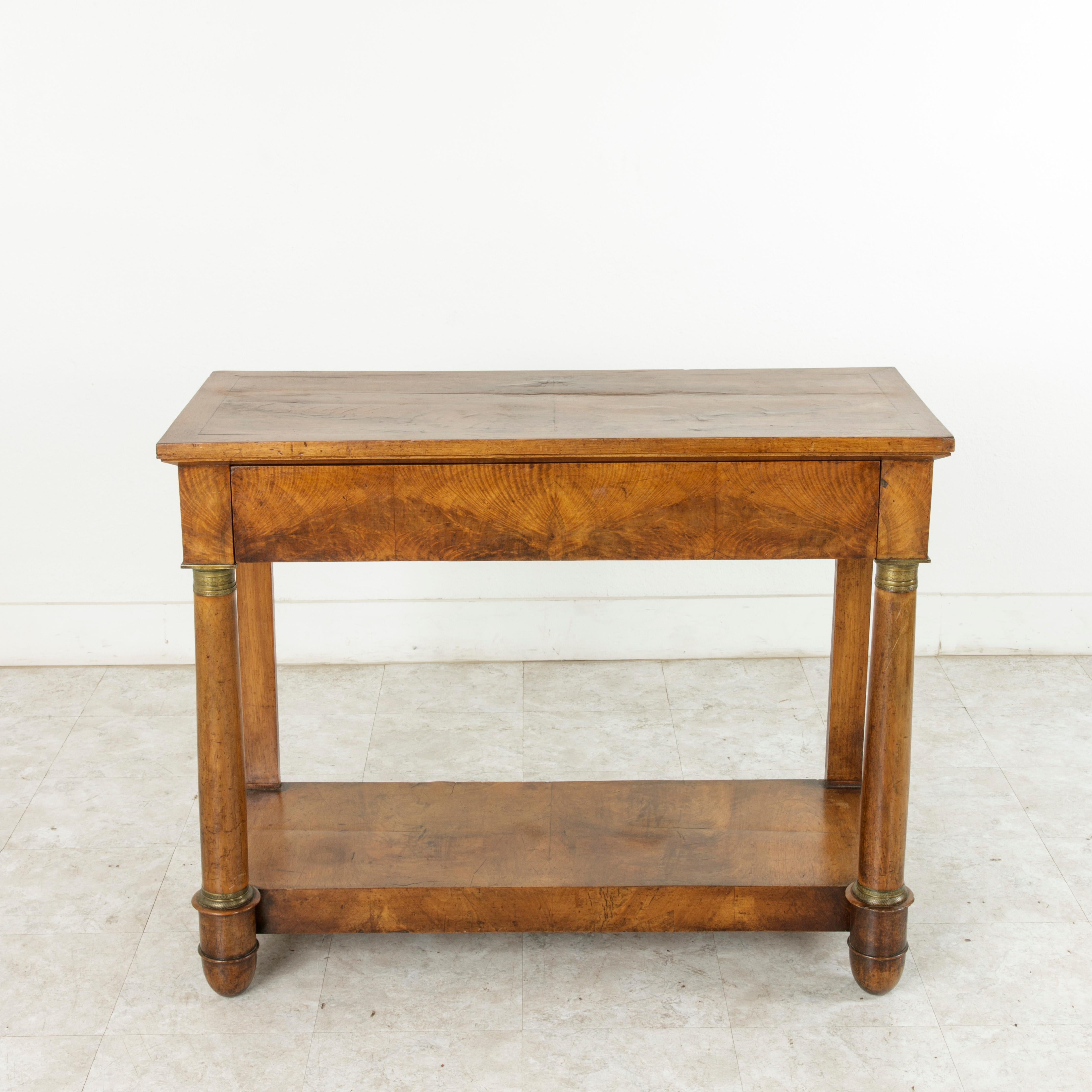 This early 19th century, French Empire period console table features a facade of beautifully book matched burl walnut. Its two columns at the front are detailed with bronze capitals decorated with a papyrus and Greek key motifs. The bronze collars
