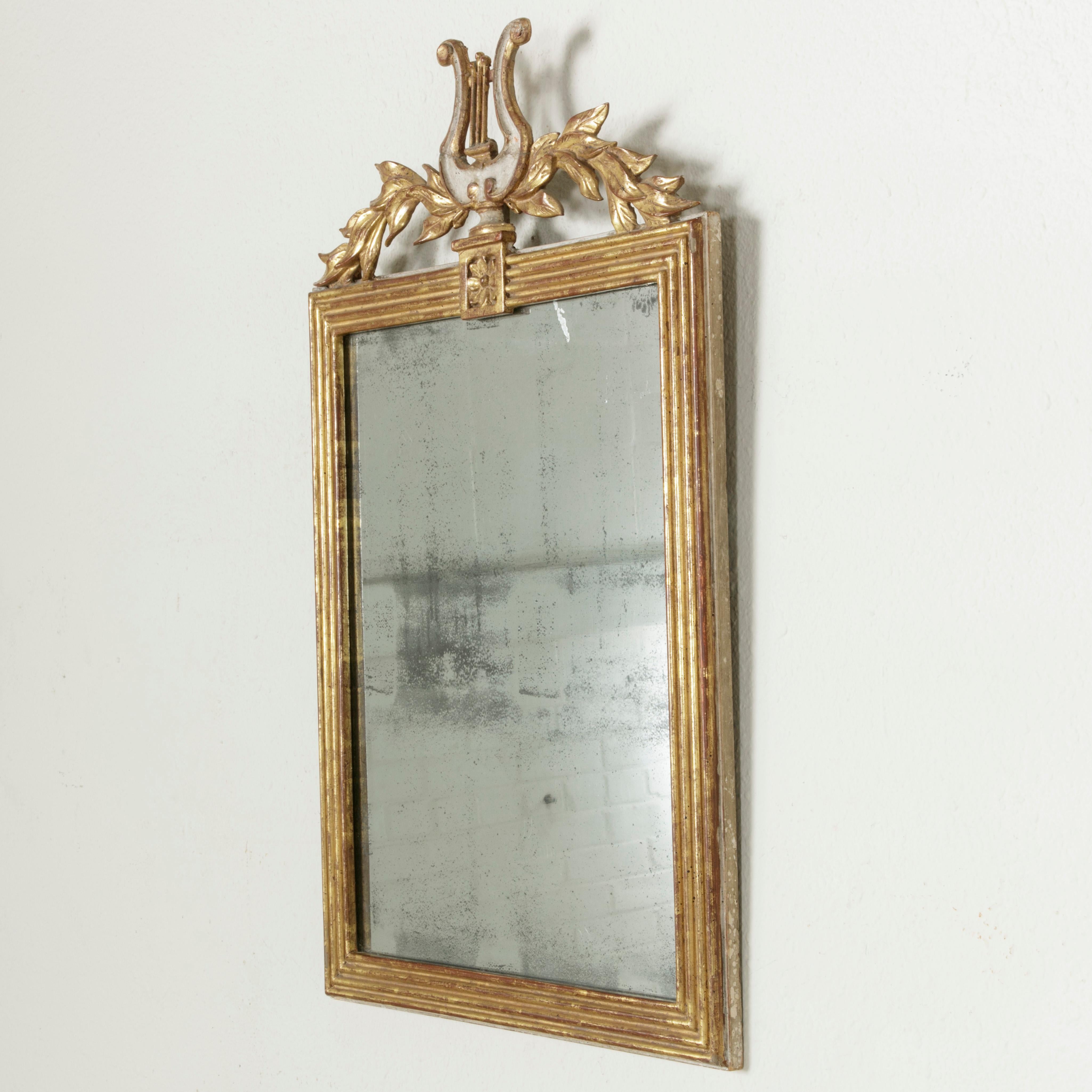 From the time of Napoleon Bonaparte, this French Empire period giltwood mirror from the early 19th century features a sculptural lyre flanked by laurel branches. Its original mercury glass is surrounded by a square fluted frame with a single rosette