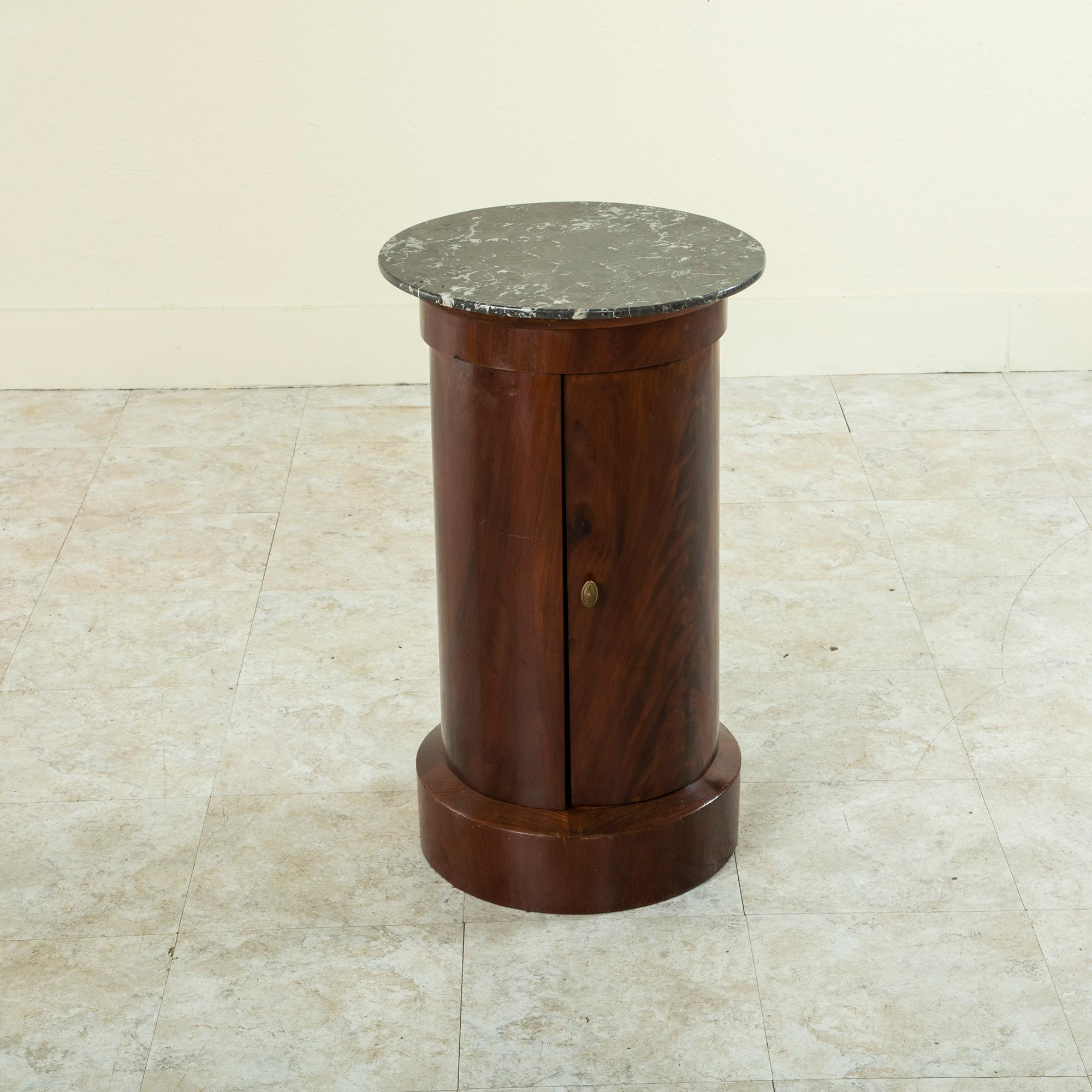 This handsome French Empire period mahogany somno or drum table features a Saint Anne marble top and a hinged curved door with bronze pull. Its cylindrical form and clean lines lend a refined yet modern character. Its interior has two shelves one of