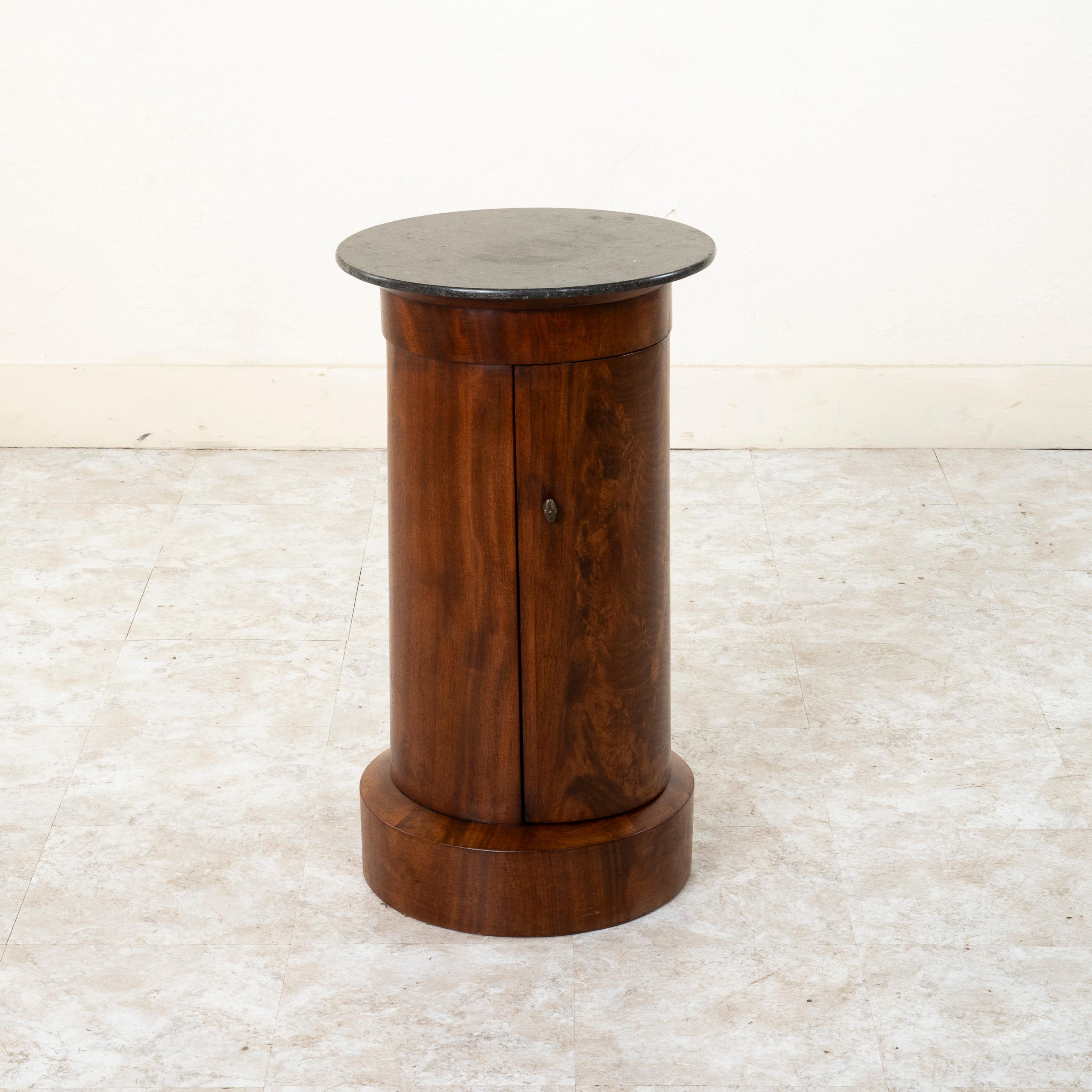 This handsome French Empire period mahogany somno or drum table features a black marble top and a hinged curved door with bronze pull. Its cylindrical form and clean lines lend a refined yet modern character. Its interior has two shelves one of