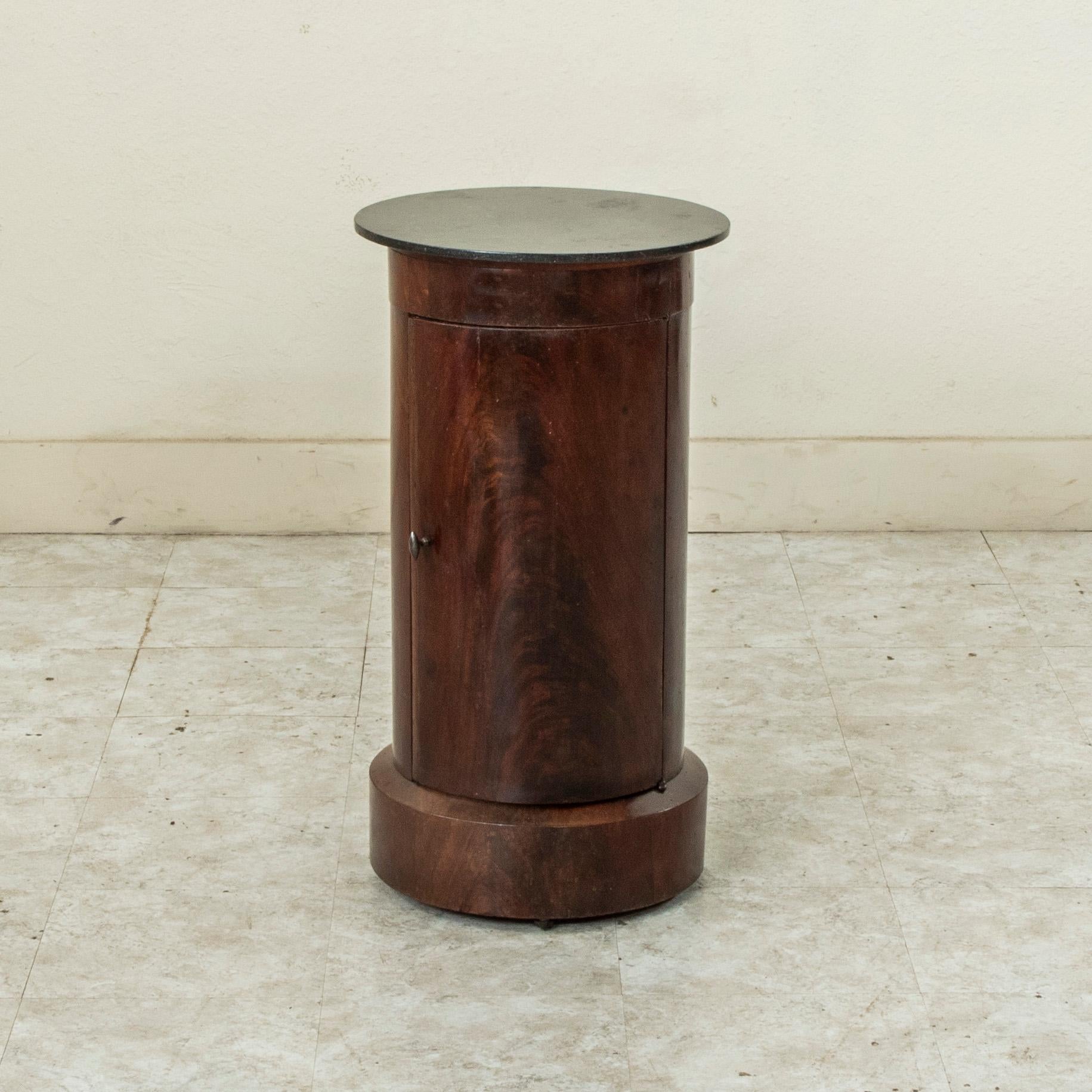 This early nineteenth century French Empire period mahogany somno or drum table features a black marble top and a hinged curved door with bronze pull. Its cylindrical form and clean lines lend a refined yet modern character. Its interior has two