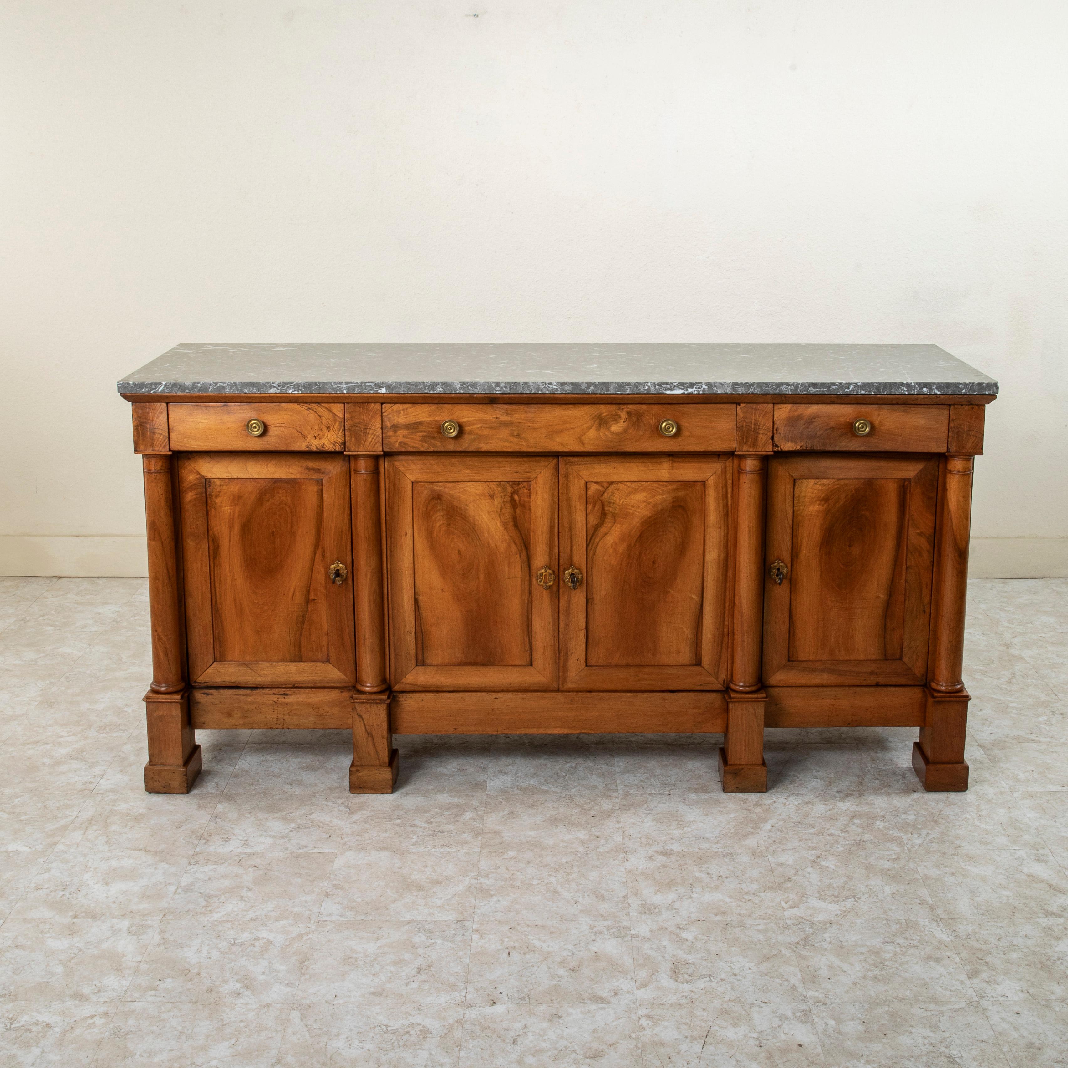 This early nineteenth century French Empire period enfilade, sideboard, or buffet features a grey marble top and is constructed of solid walnut. Four columns flank the doors of the facade. Three drawers of dovetail construction fit into the apron