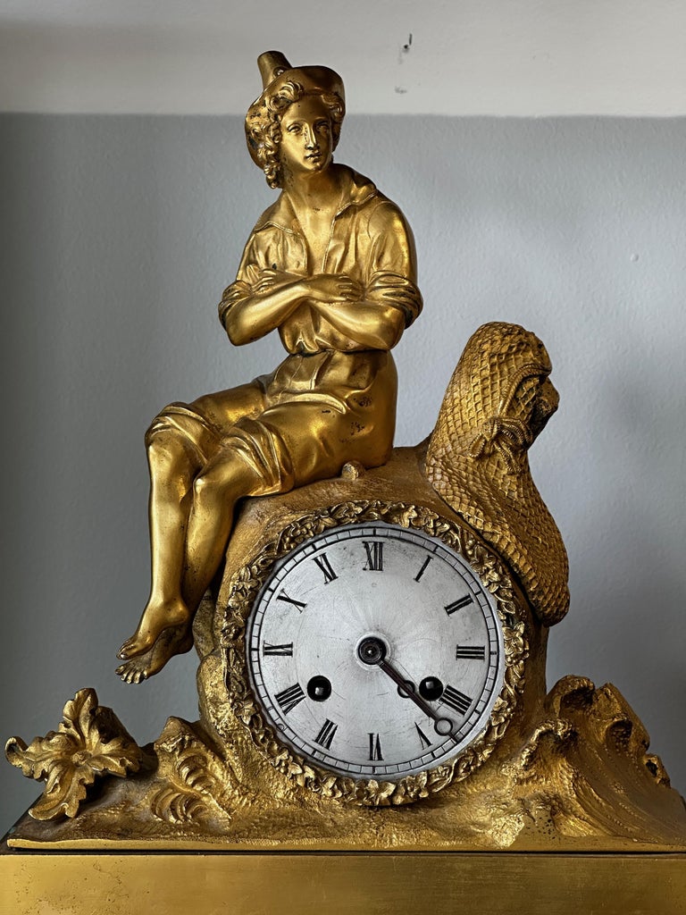An early 19th C. French Empire gilt bronze figural clock, depicting a young fisherman sitting on a rock with his net draped beside him with waves crashing at his feet.