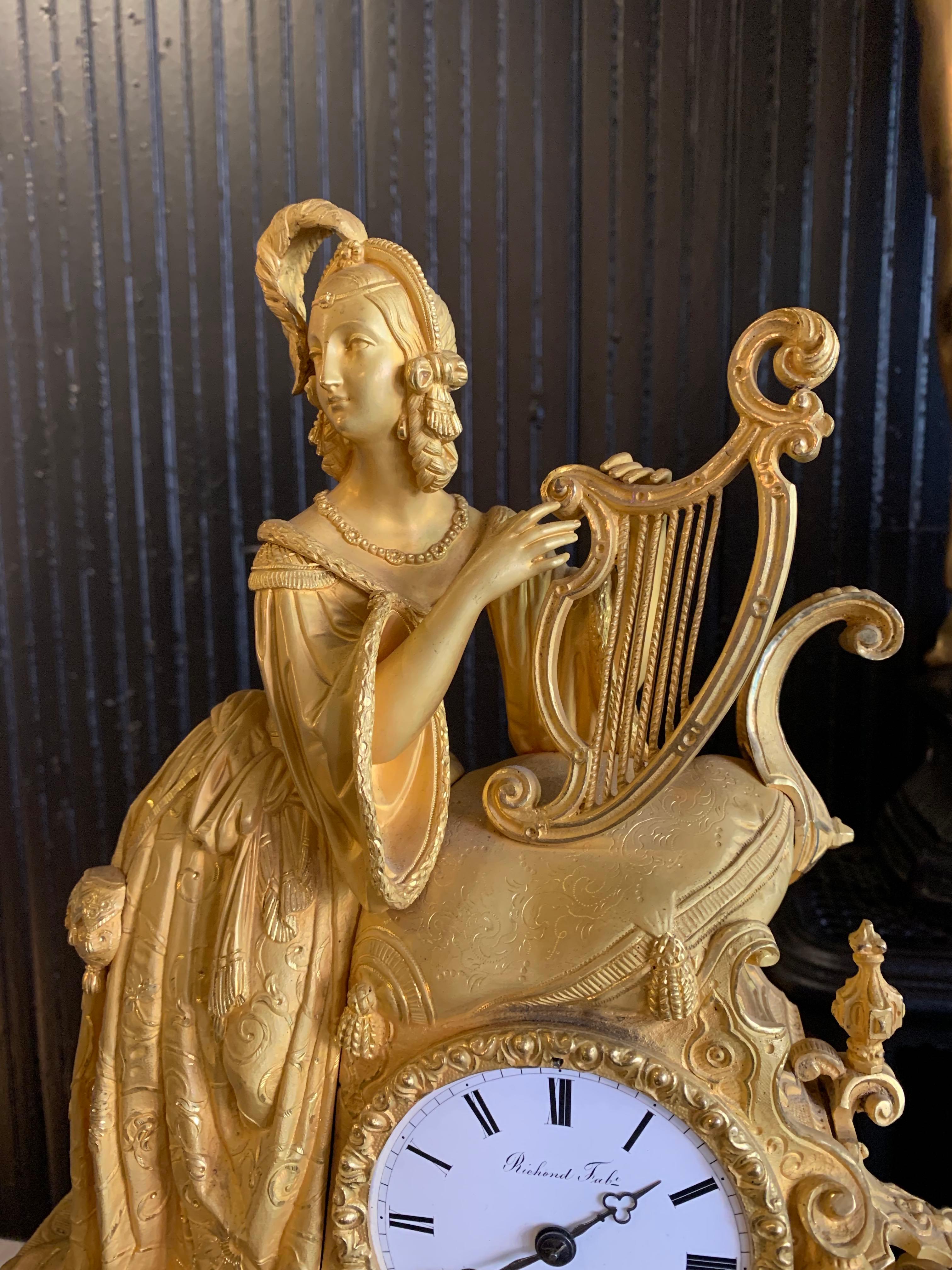 Louis XVI Rococo style ornate mantle clock with figure of an 18th century dressed woman playing the harp.