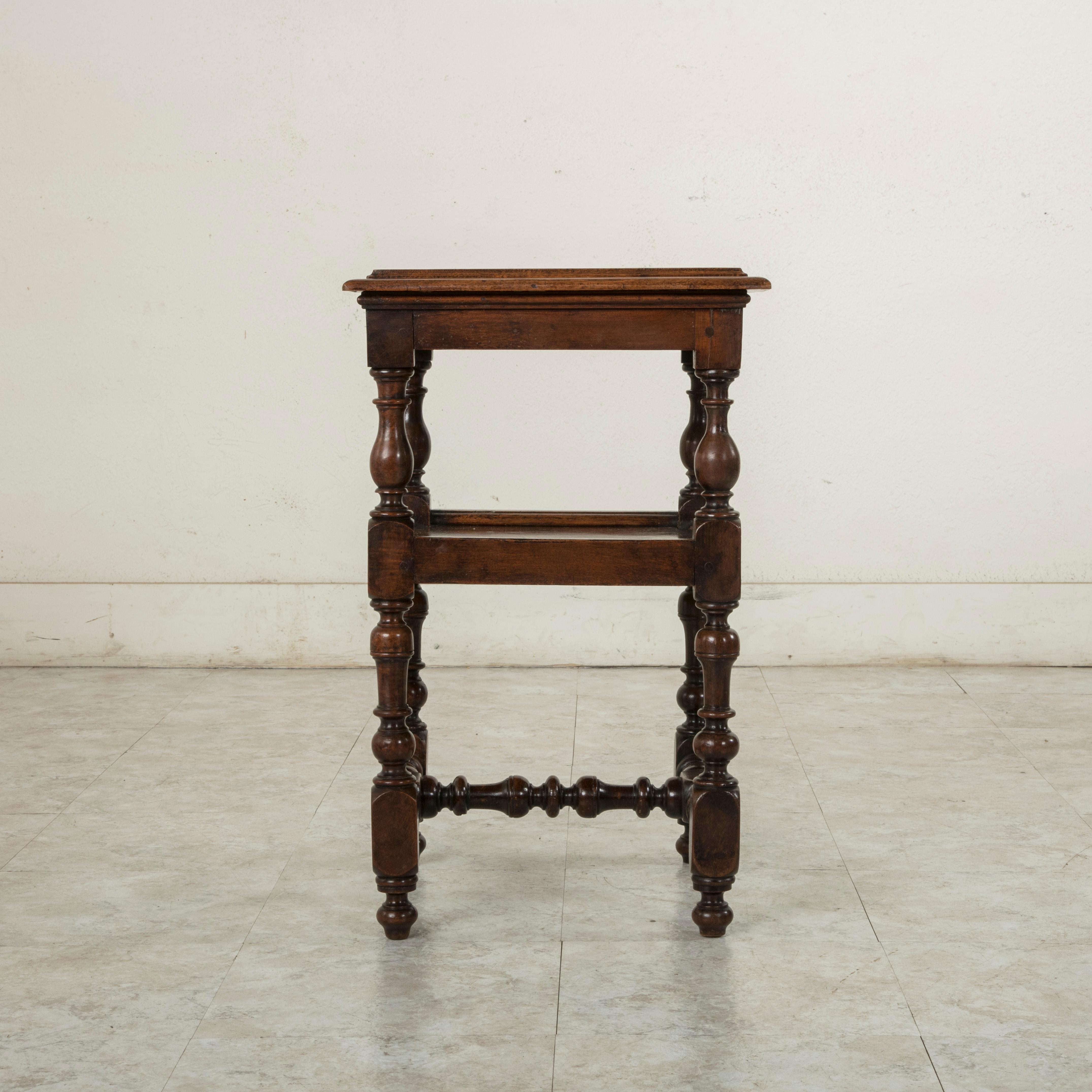 This early 19th century French Louis XIII style walnut side table features hand pegged construction and a beveled top. A lower shelf provides additional display space. Its turned legs are joined at the base by an H-stretcher, circa 1800.