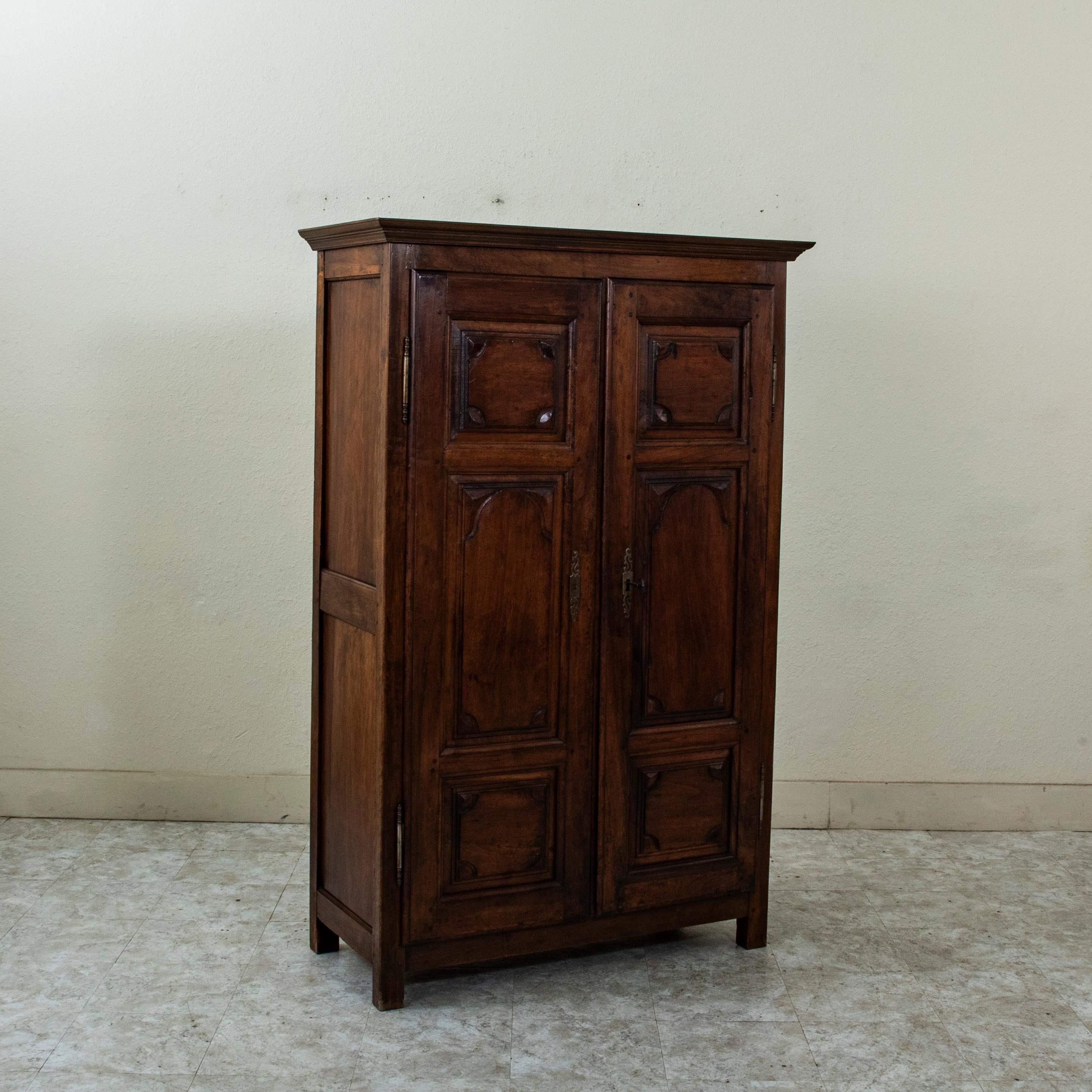 This small scale early nineteenth century French walnut armoirette or wardrobe features hand pegged paneled sides and doors. The piece is crowned with a multi-beveled cornice. Its two doors are classic Louis XIV style in design with symmetrical