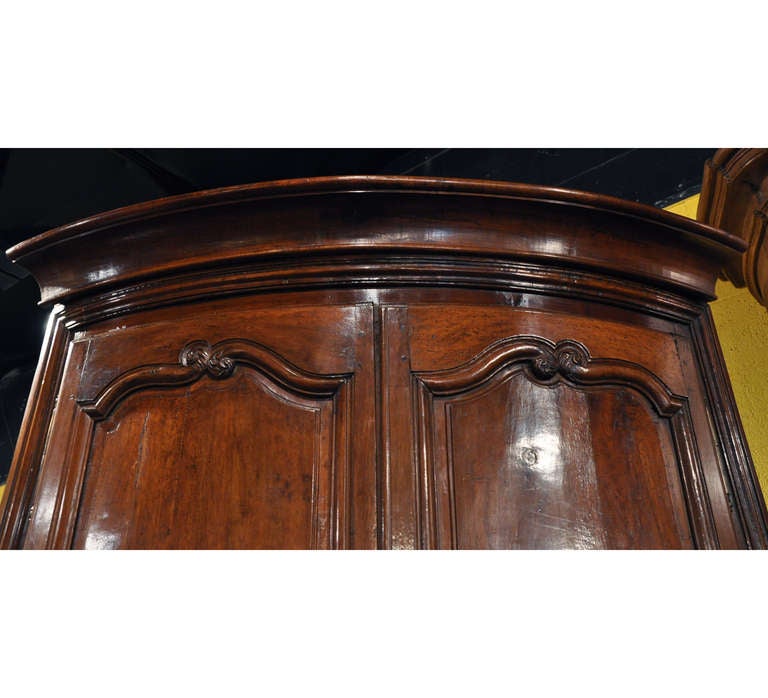 Cette grande et élégante encoignure (ou armoire d'angle) Régence en bois fruitier à façade en arc a été fabriquée dans la région du Poitou en France, vers 1810. Posé sur des pieds à volutes sous un tablier festonné, ce meuble ancien est construit en