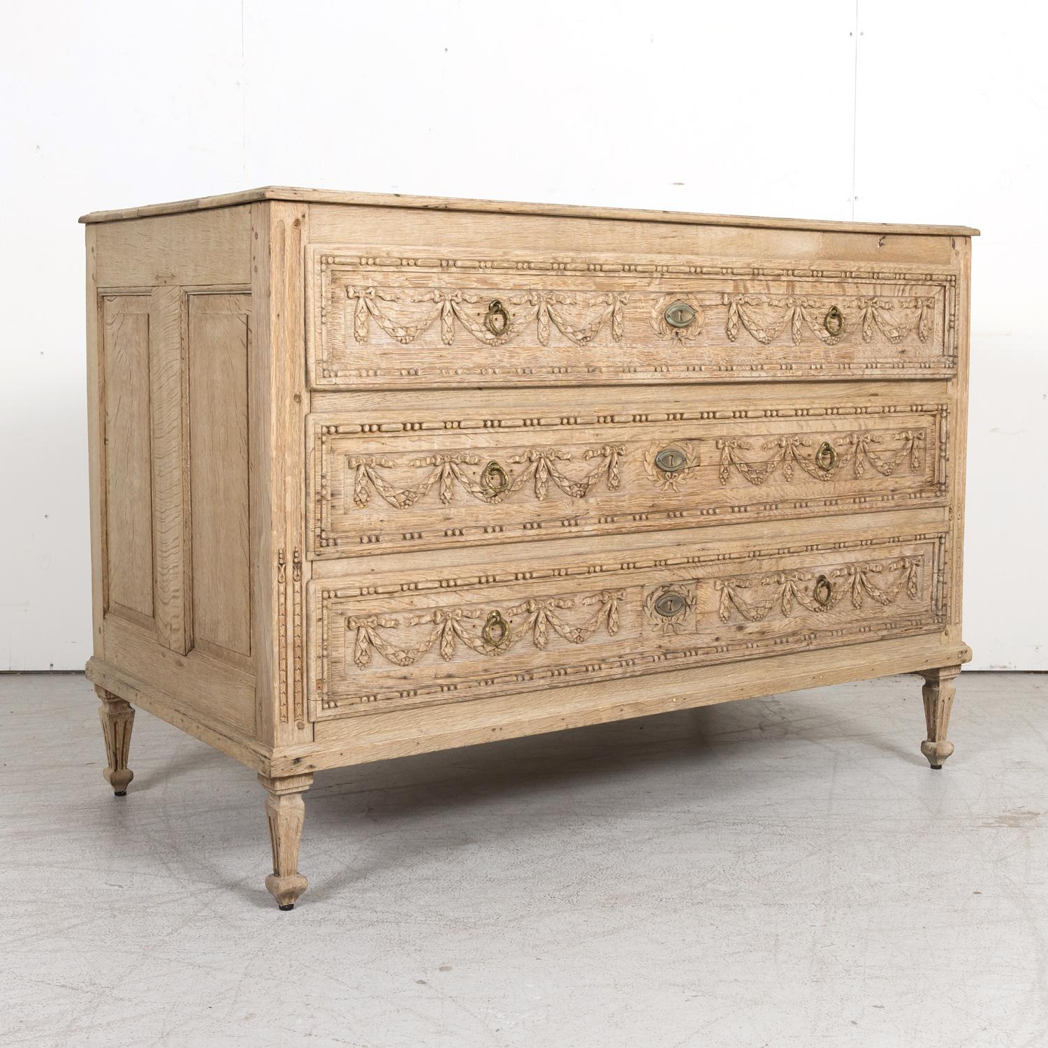 An early 19th century French Louis XVI style carved commode handcrafted of solid oak by talented artisans near Aix-en-Provence in the Provence region of southern France, circa 1810. This exquisite bleached wood commode features a rectangular plank