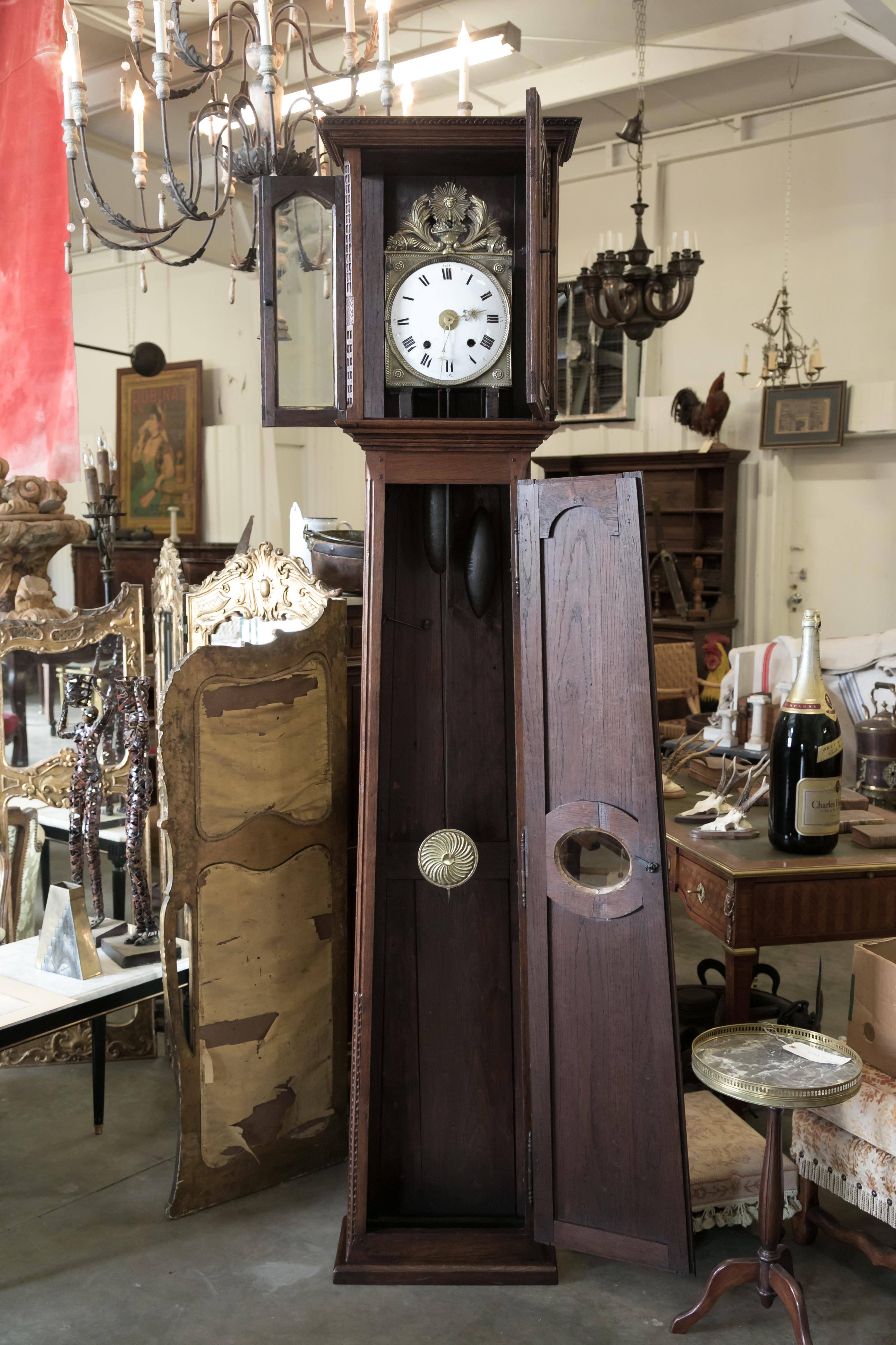 Antique French Louis XVI style 8-day longcase clock, circa early 1800s. The case of this handsome longcase clock was hand crafted of solid oak in Normandie. It houses an enameled dial with Roman numerals and stamped brass hands. Pediment fronton of