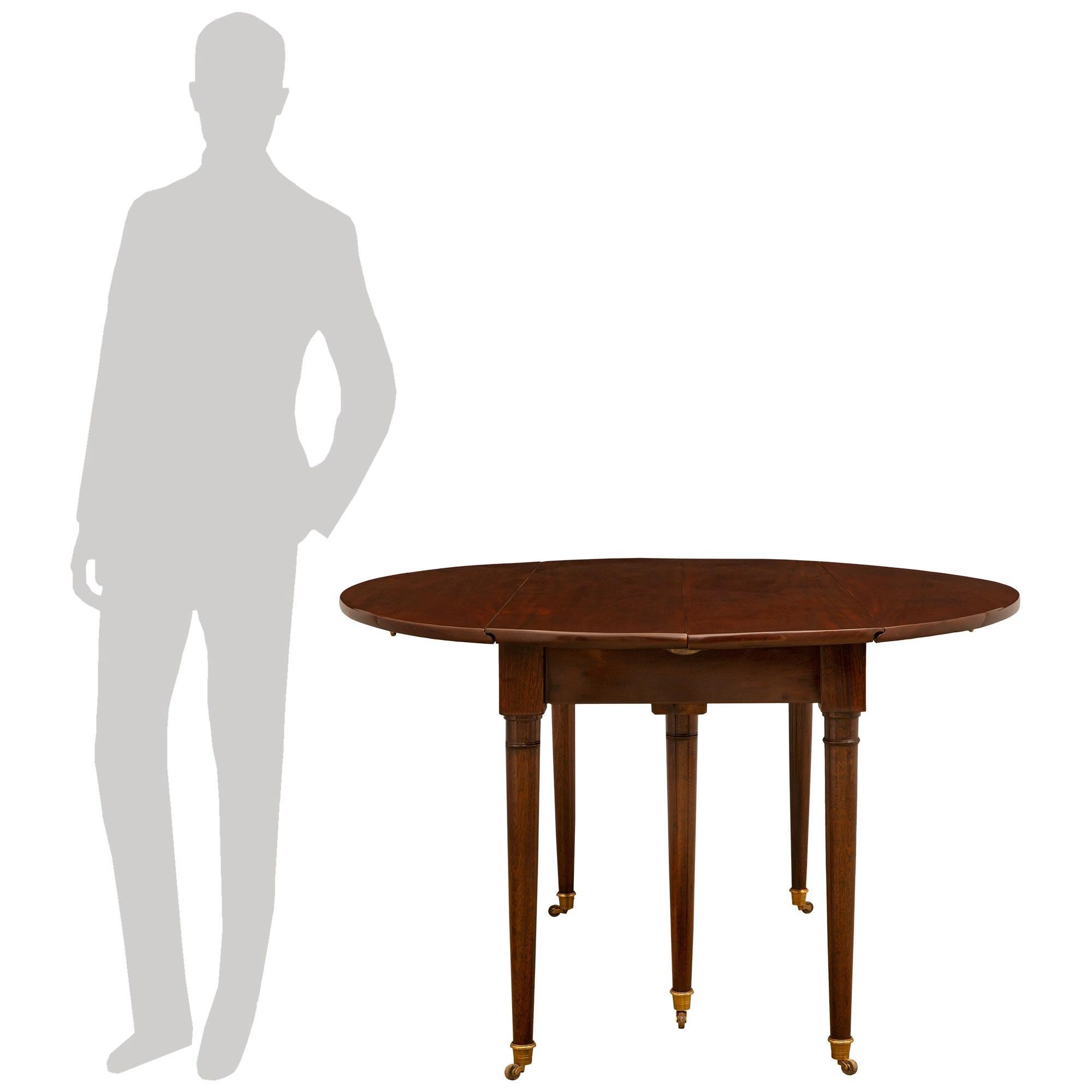 Très élégante table de salle à manger de style Louis XVI en acajou, datant du début du XIXe siècle. Elle repose sur six pieds circulaires fuselés terminés par des sabots en bronze doré et des roulettes en bois d'origine. Aux deux extrémités de la