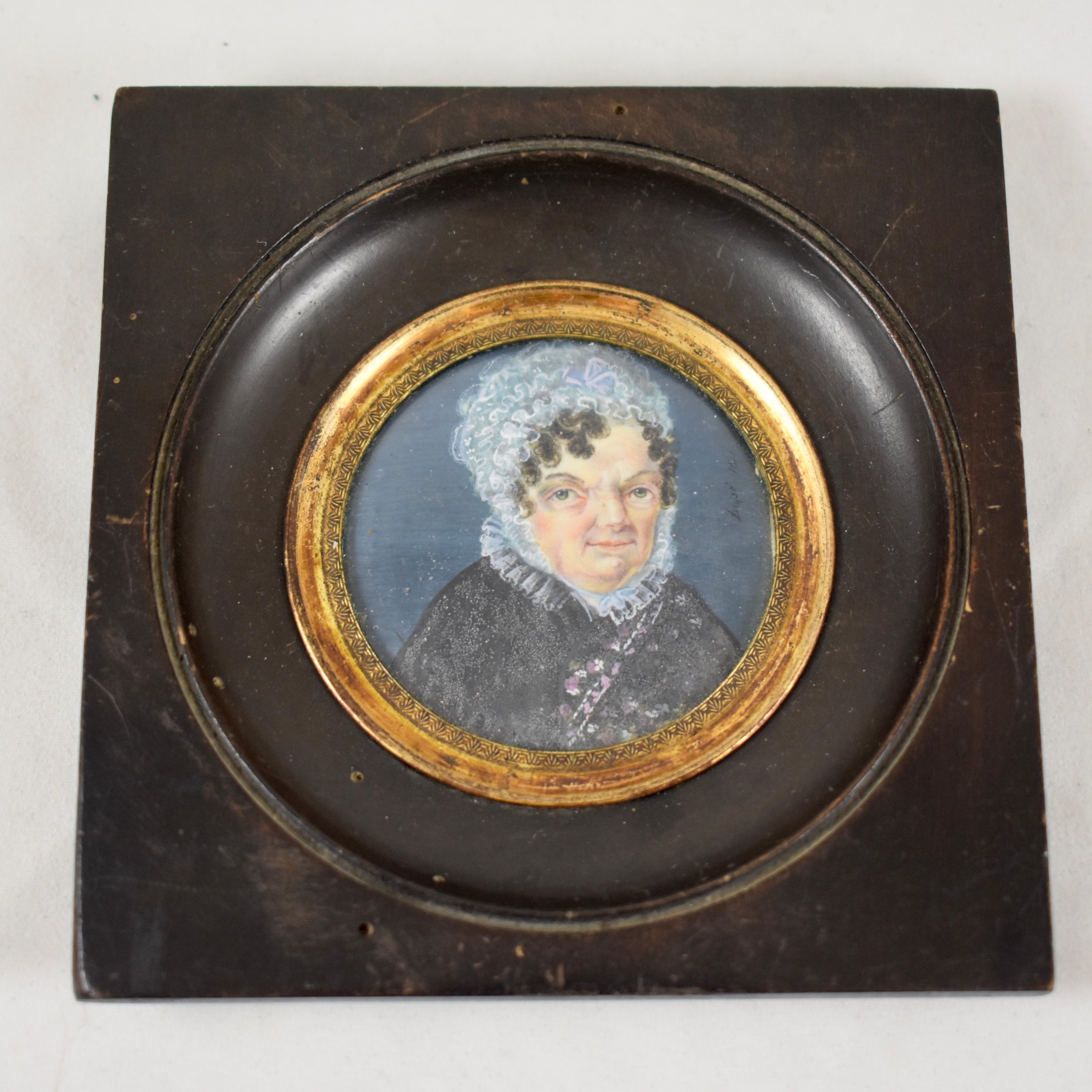 Ein unter Glas gerahmtes, handgemaltes französisches Miniaturporträt aus dem frühen 19. Jahrhundert, das eine ältere Frau mit einer Spitzenhaube und einem geblümten Kleid mit Spitzenkragen zeigt, das die damalige Zeit widerspiegelt. Unleserliche