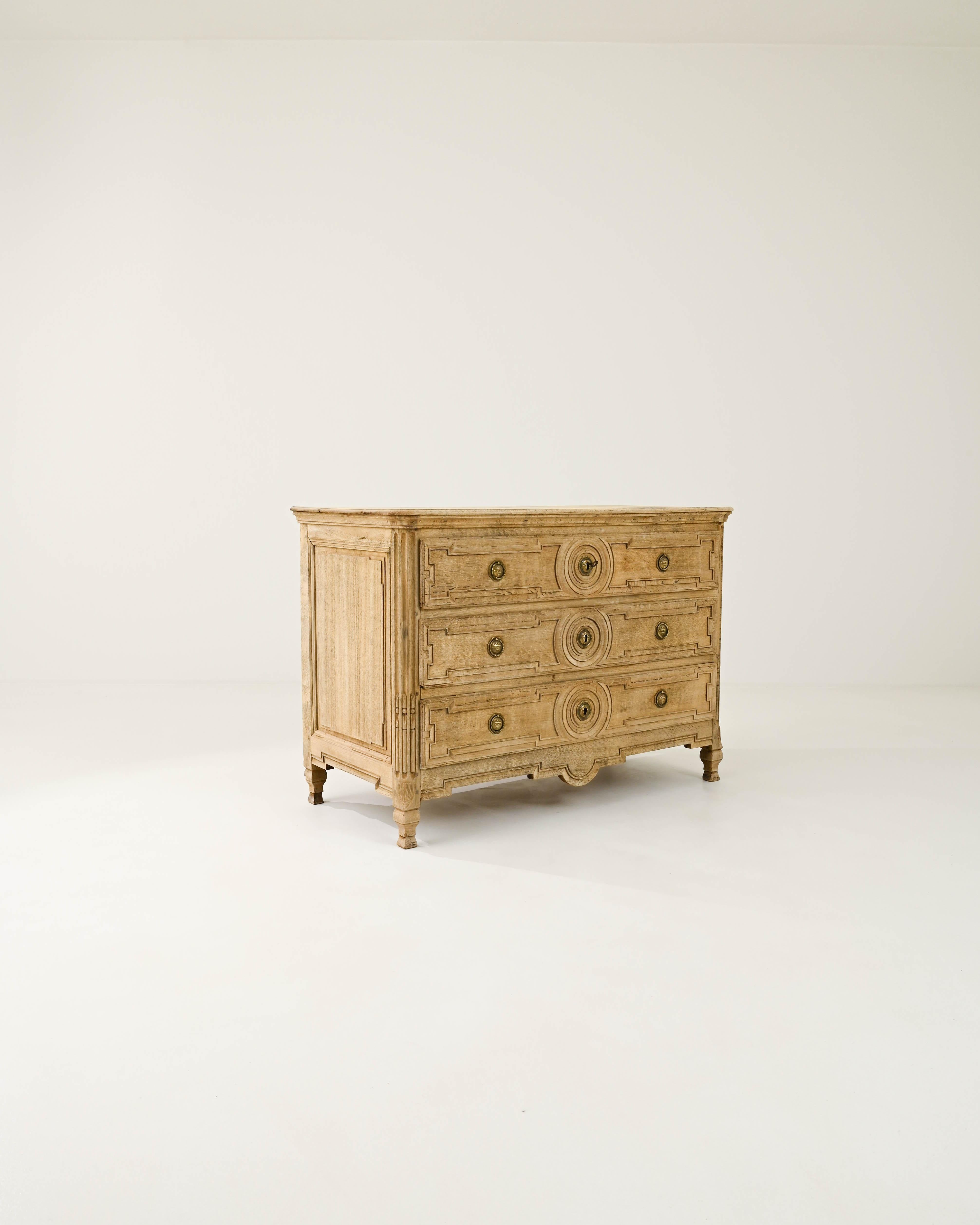 Graceful and refined, this antique chest of drawers offers a Neoclassical design in natural oak. Hand-built in France in the early 1800s, the paneling of the drawers is precise and geometric; a circular motif in the center of each panel creates a