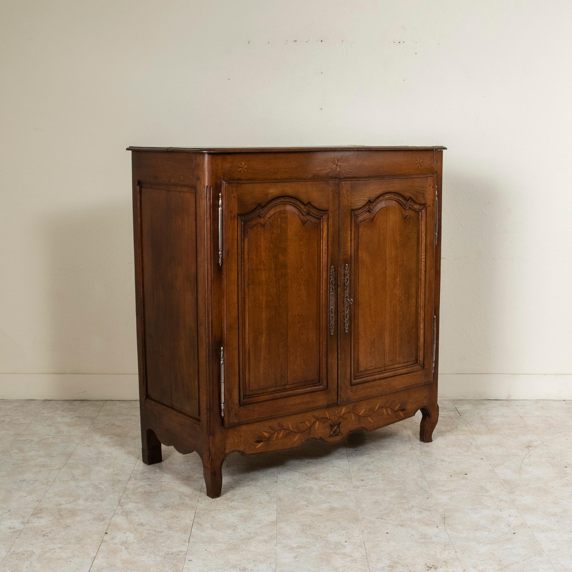 From the town of Bazoches in the Le Perche region of Normandy, France, this hand carved oak bassette or petite armoire from the early 19th century is detailed with inlaid exotic woods depicting vines, leaves and stars. Its two paneled doors on iron