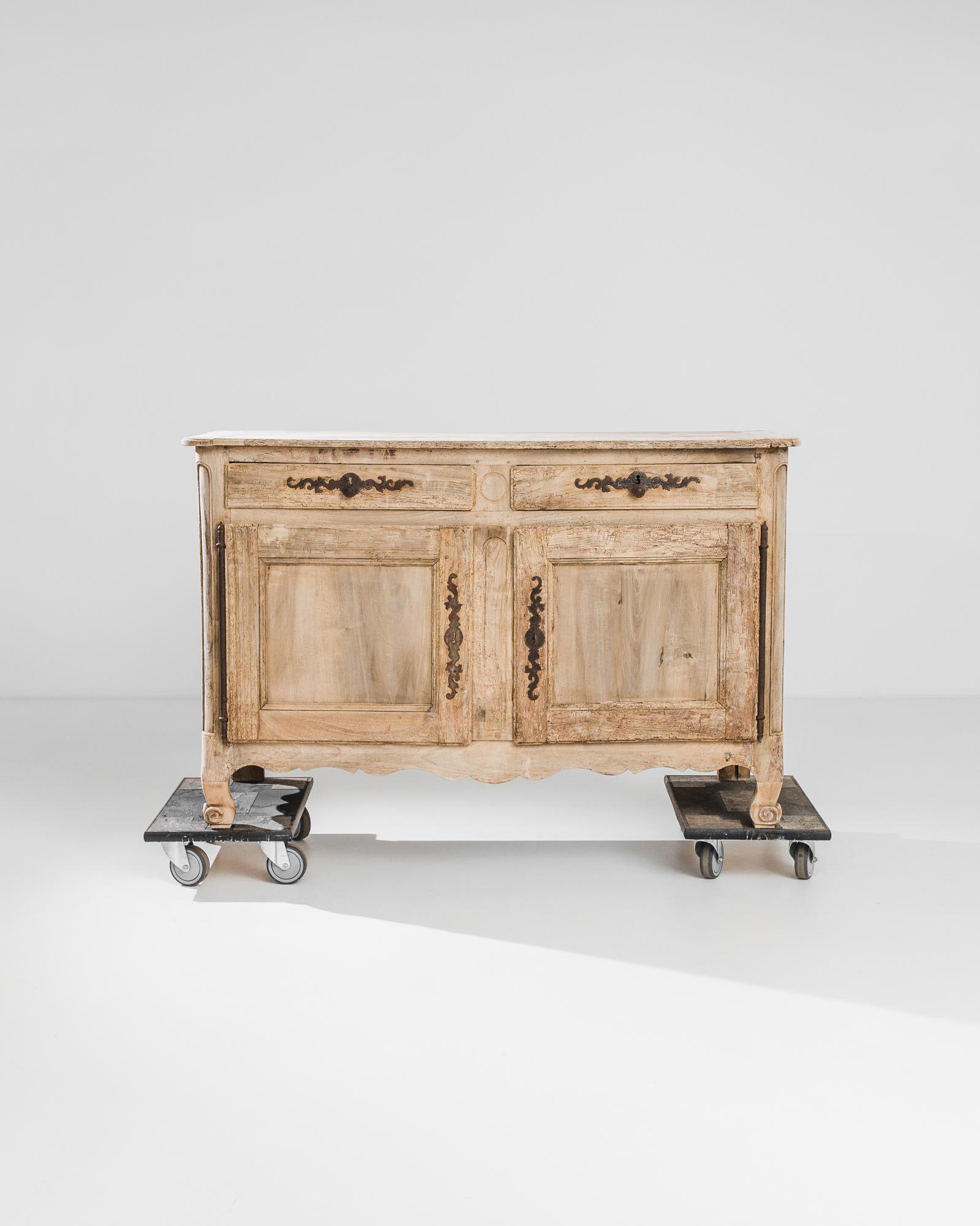 Romantic lock pieces and carved detail give this French country buffet an enchanting character. Made circa 1800, the upright shape of the case is enlivened by scrolled feet and a scalloped apron. An oxidized patina dapples the elaborate tendrils of