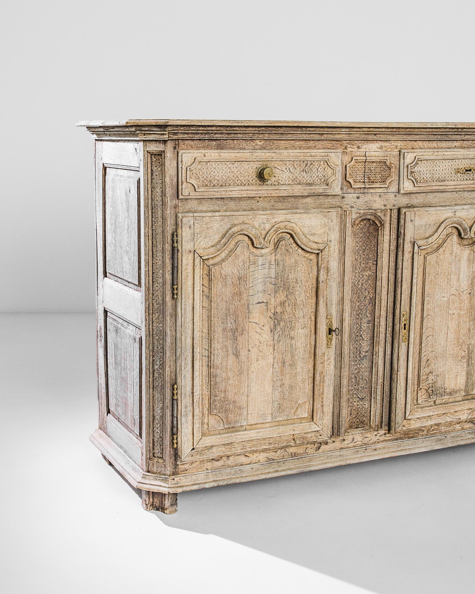 Handcrafted circa 1800 in France, this exquisite bleached oak buffet features two drawers resting over two panel doors with original brass hardware —a doorknob and three ornate locks. Top drawers and the spaces between the doors are decorated with a