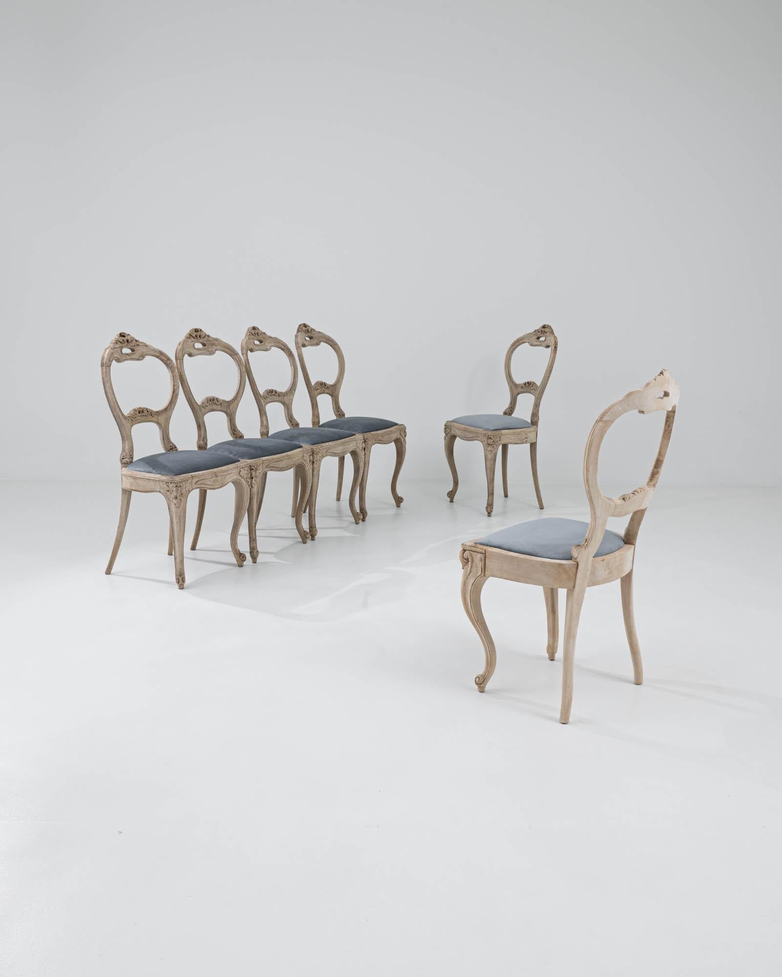 Handcrafted in early 19th-century France, these dining chairs captivate with their graceful, curvilinear silhouettes. The round backrests feature exquisitely carved foliate details that harmonize with the elegant curves of the cabriole legs,