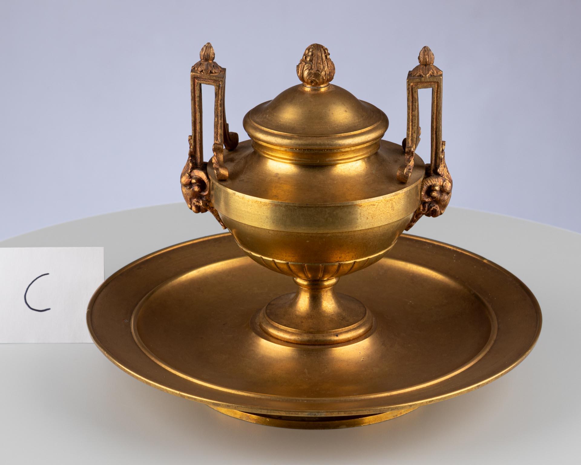 Encrier Empire sur base circulaire

Origine : France
MATERIAL : Bronze doré (Ormolu)
Date : Circa 1800-1810

Dimensions :
H × D&H : env. 16 × 19 cm

Description :
Encrier de style classique en forme d'urne à couvercle, monté sur une base circulaire.