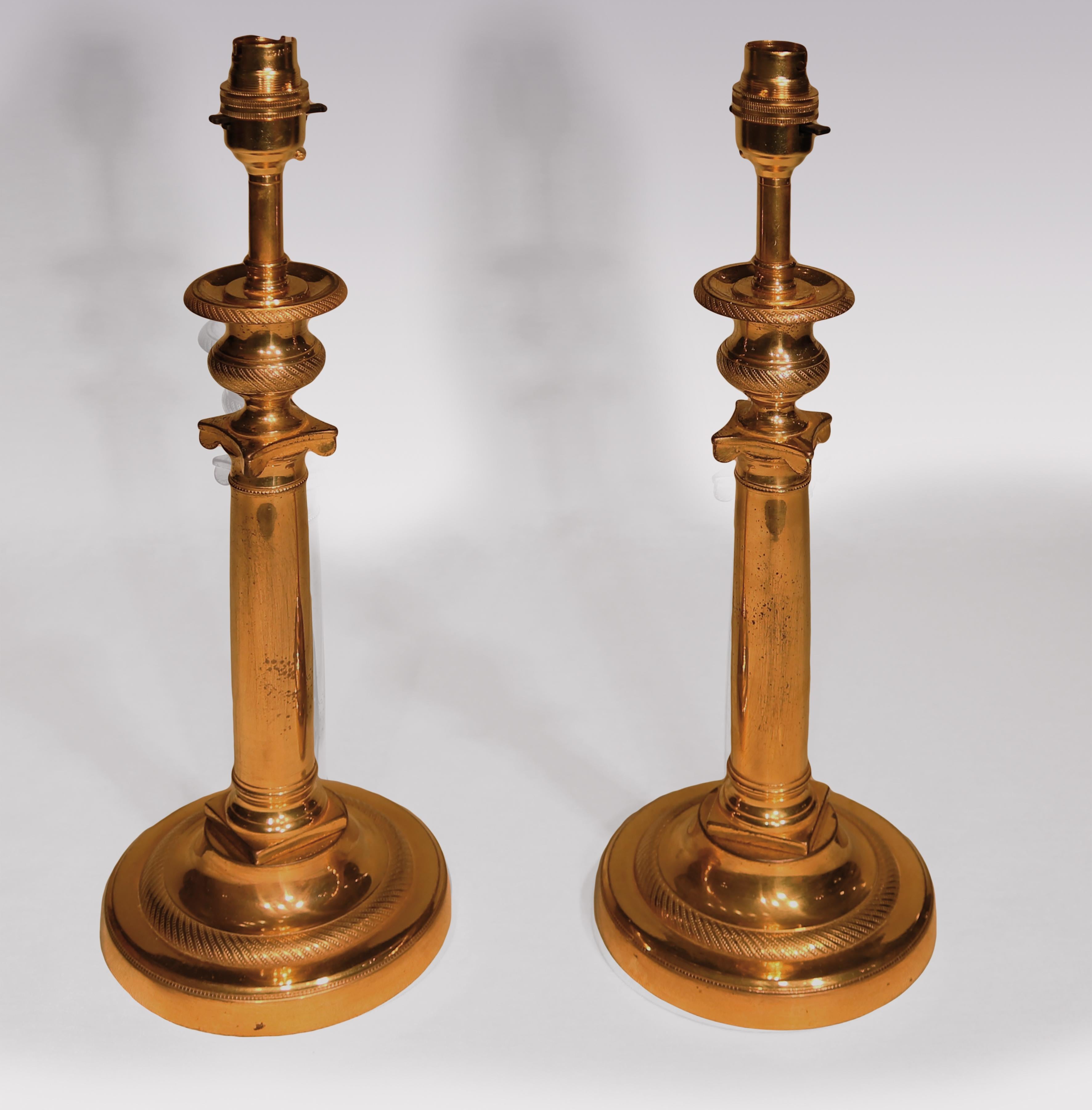A pair of early 19th century French ormolu candlesticks having engine-turned vase-shaped nozzles, raised on Ionic capital columns supported on engine-turned circular plinth bases.
(Now converted to lamps).