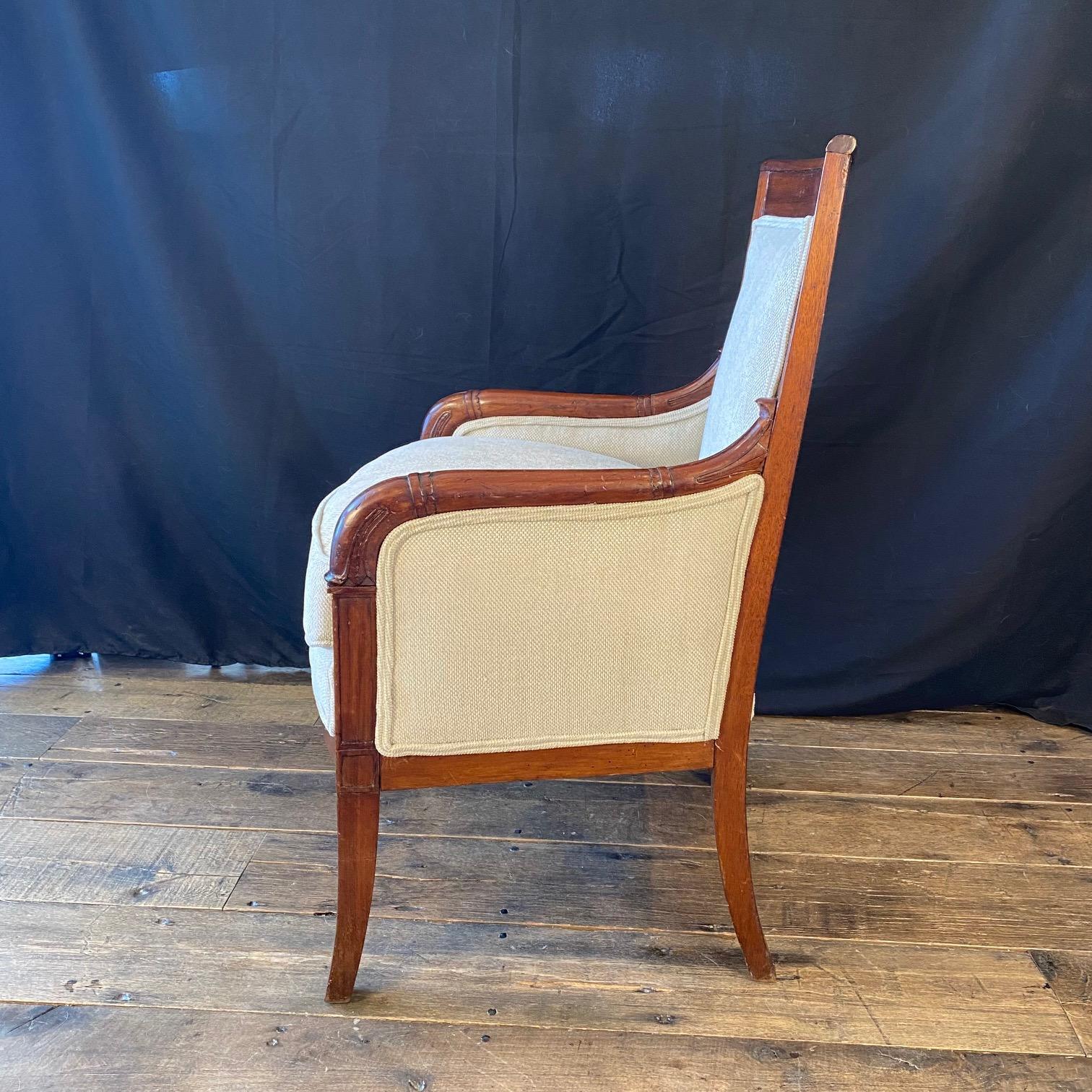 Elegant pair of French Empire fauteuils or armchairs from the early 19th century, having coved square backs with scroll arms enriched with stylized acanthus leaves and florets, all standing on scroll legs at the front and straight saber legs in the