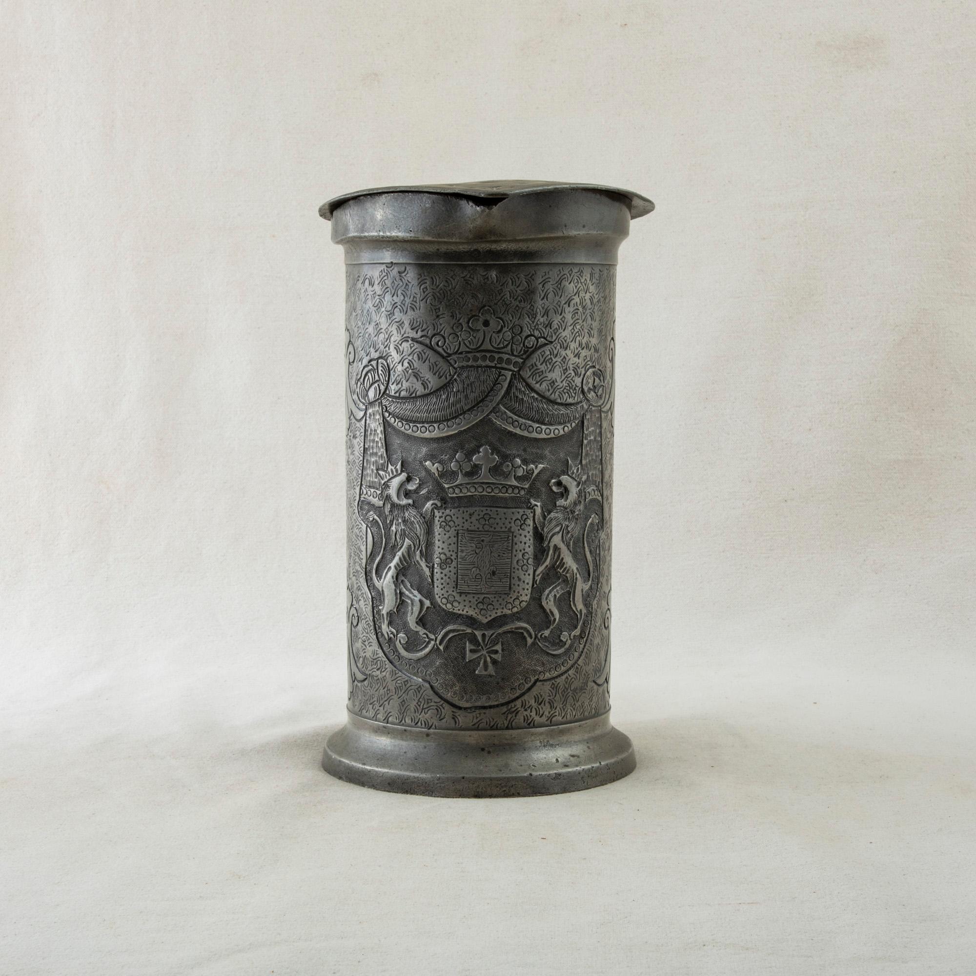 Standing at 10 inches in height, this large early nineteenth century French pewter tankard features a coat of arms with an eagle flanked by crowned lions. Below the coat of arms is a cross and above is a crown. An additional crown with dais