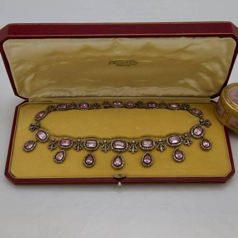 An antique and rare pink topaz and diamond, gold and silver necklace in its red leather case.
Front set with 14 faceted rectangular pink topaz framed by antique-cut diamonds alternating with diamonds palmettes and supporting seven pear-shaped pink