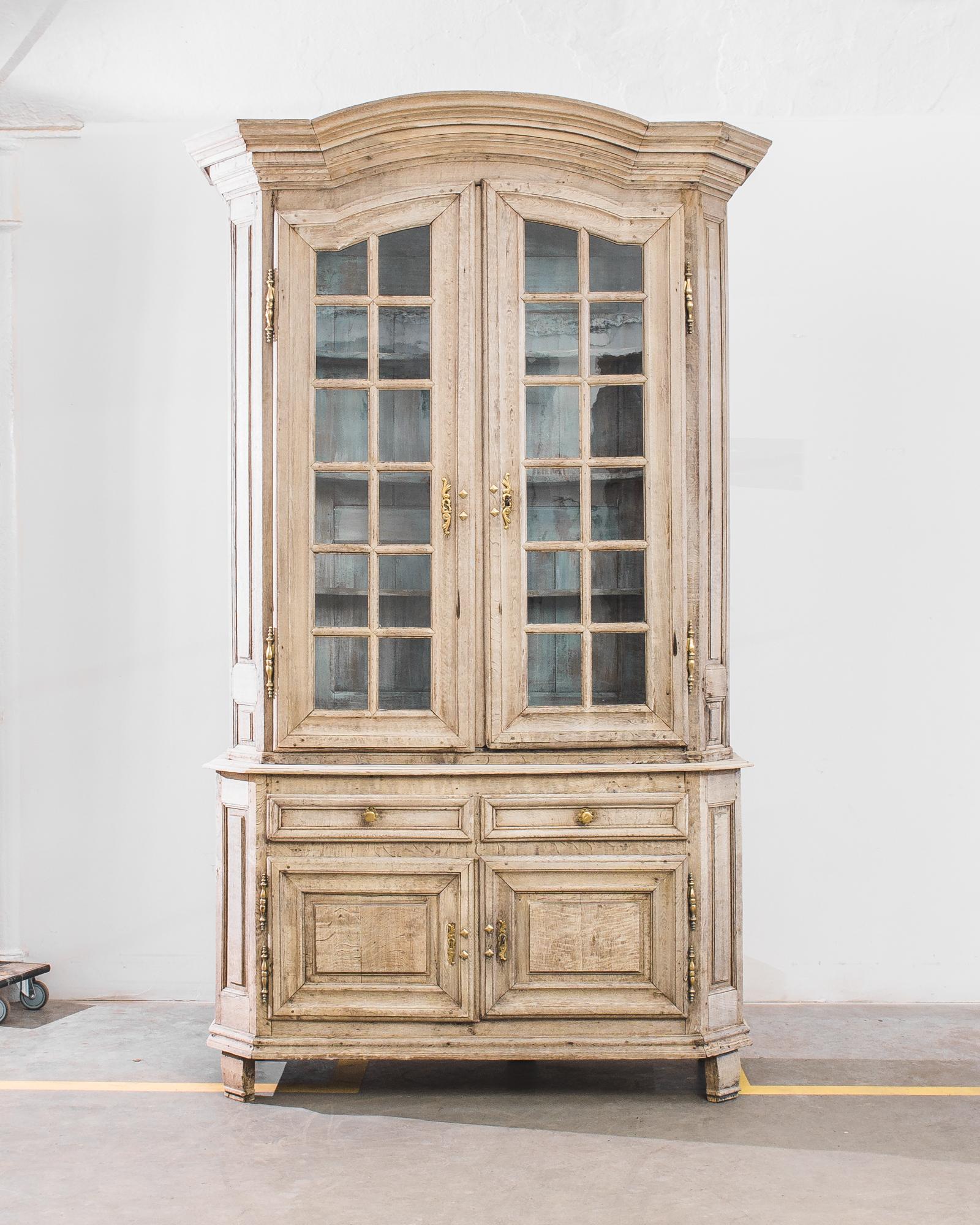Defined by characteristics of simplicity, taste and functionality, this French à deux corps bleach oak vitrine was assembled circa 1800. Boasting two tall glass doors resting over a commode with two drawers and raised panel doors. A curious touch: