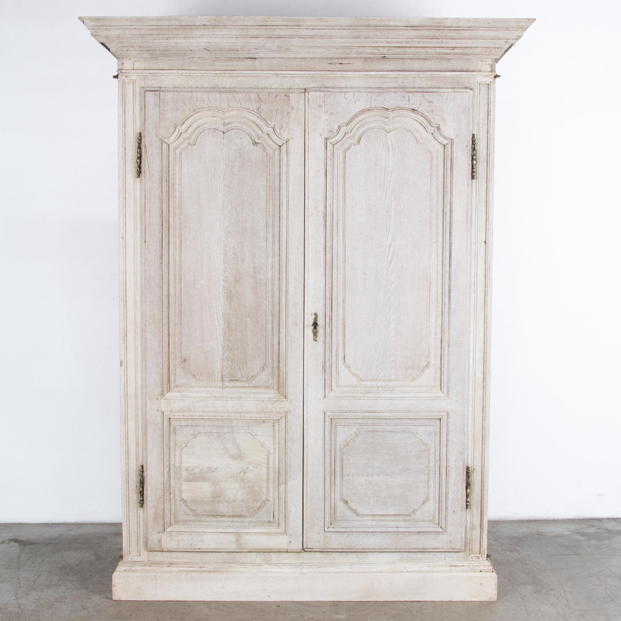 A spacious wardrobe from France, circa 1800. Time tested traditional craftsmanship, with distinctive cold growth oak in a rustic neutral finish and original brass hardware. A practical and beautiful storage piece with interior drawers and elaborate