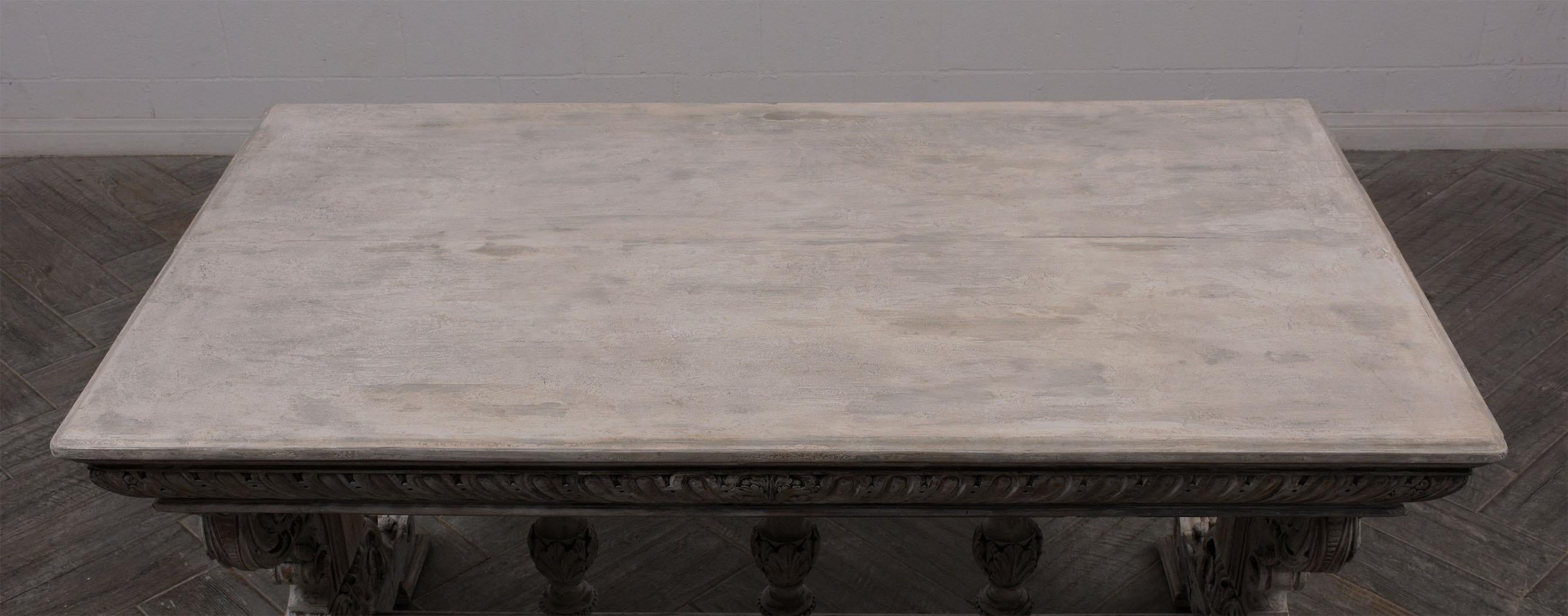 This 19th Century French Renaissance Library Table is made of walnut wood and has been newly painted in an off white color with a distressed finish. This Writing Table features heavily carved motif details along the stretched pedestal legs and three
