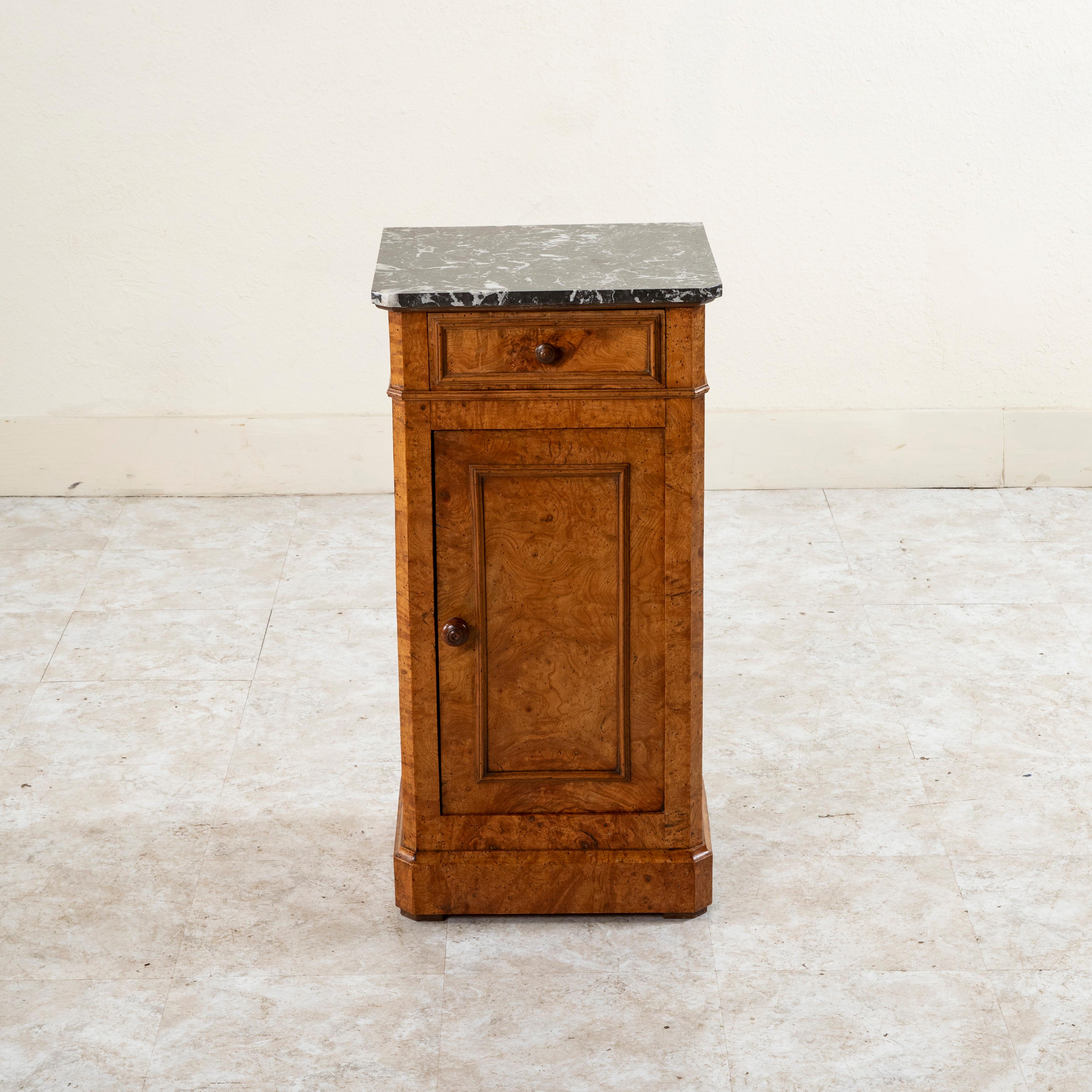 This early nineteenth century French Restauration period burl elm nightstand or side table features a Saint Anne marble top. It has a single drawer of dovetail construction, and the door below opens to allow access to a cabinet with a shelf for