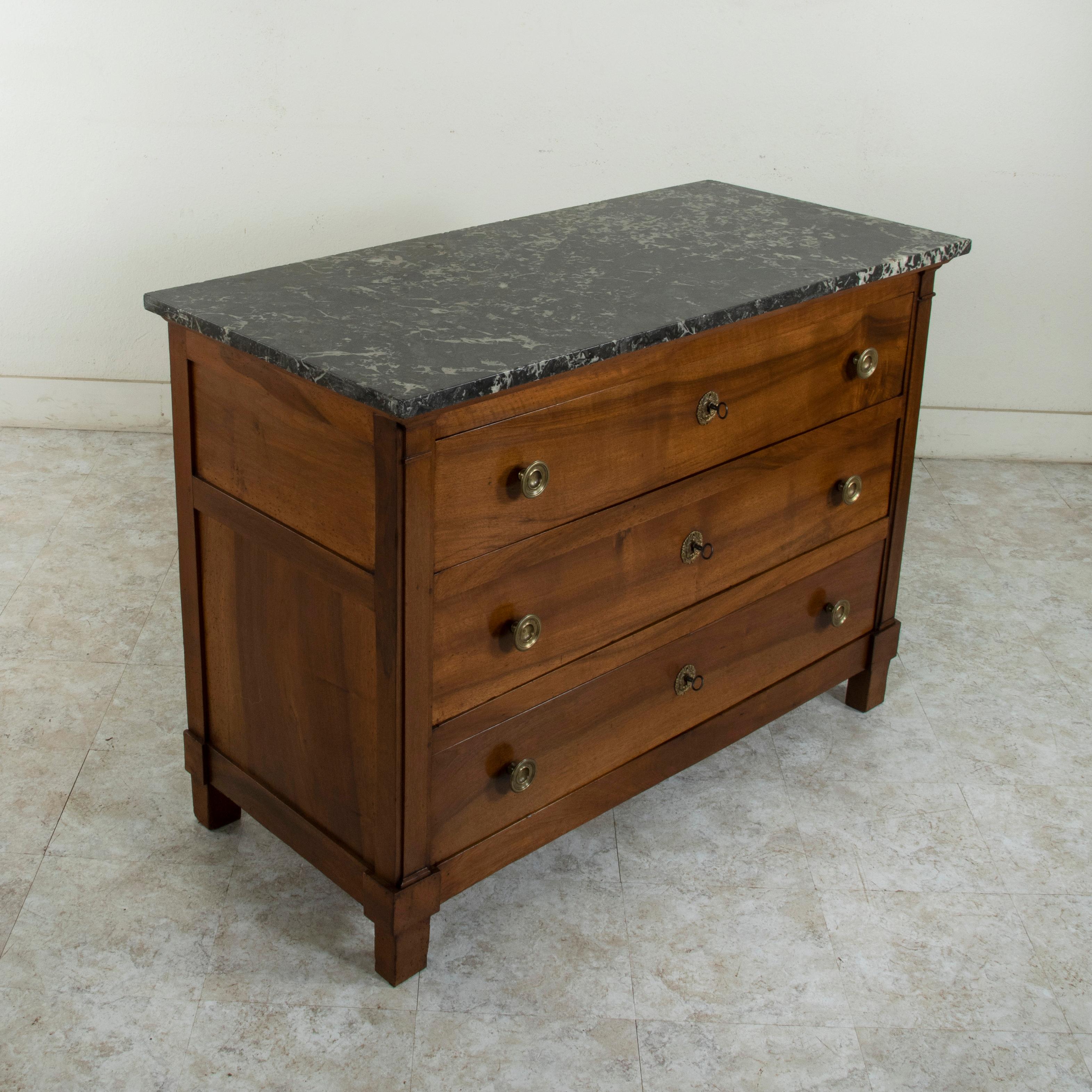 This French Restauration period walnut commode or chest of drawers from the early nineteenth century features its original Saint Anne marble top. Constructed of solid French walnut, its three drawers of dovetail construction are flanked by square