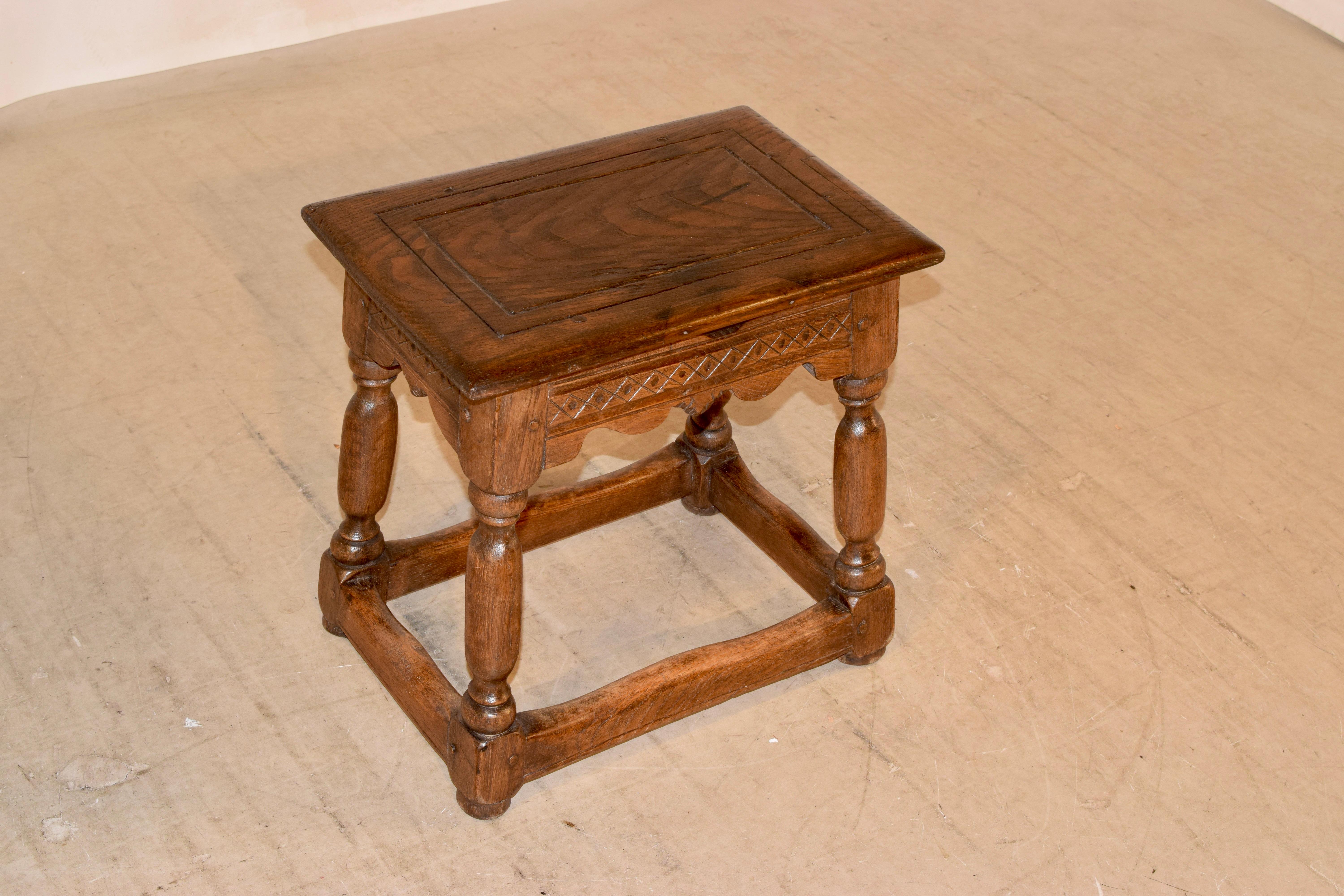 Early 19th century elm stool from France with a wonderfully grained top which has routed paneled decoration. The apron is simply elegant with hand scalloping and carved decoration and the stool is supported on hand turned and splayed legs, joined by