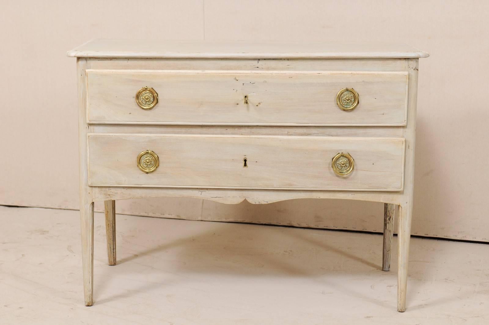 A French wooden two-drawer chest from the early 19th century. This antique French commode features a simple and clean line body which is accented with a subtly scalloped accolade style carved skirt on three sides. There are two long drawers, adorn