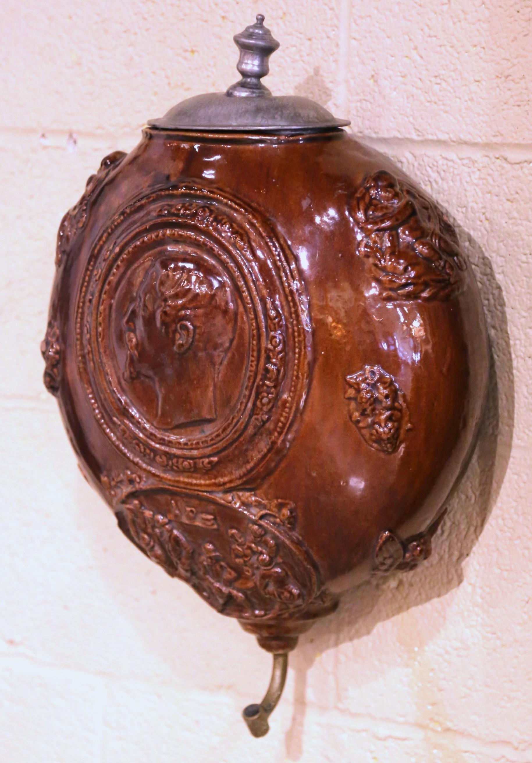 Décorez un mur d'entrée ou un couloir avec cette élégante fontaine antique en terre cuite. Fabriqué en France vers 1830, ce réservoir décoratif présente un profil masculin classique en bas-relief dans un médaillon, tandis qu'une scène de taverne