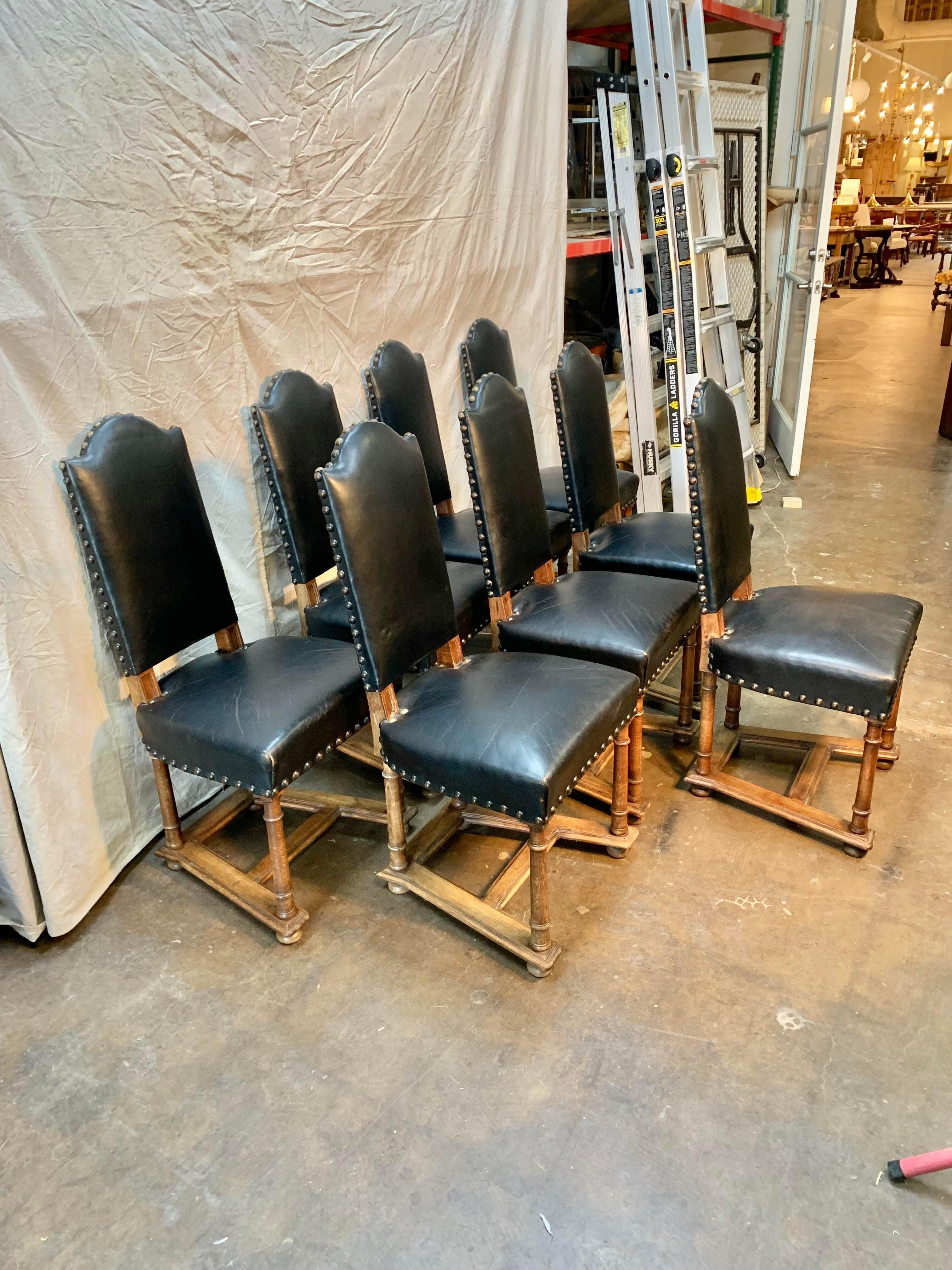 Found in France, this set of eight Early 19th Century French Dining Chairs feature the original leather upholstery and hand carved walnut. The chairs feature tall backs with nail heads. The trapezoidal shaped seats are supported by turned legs
