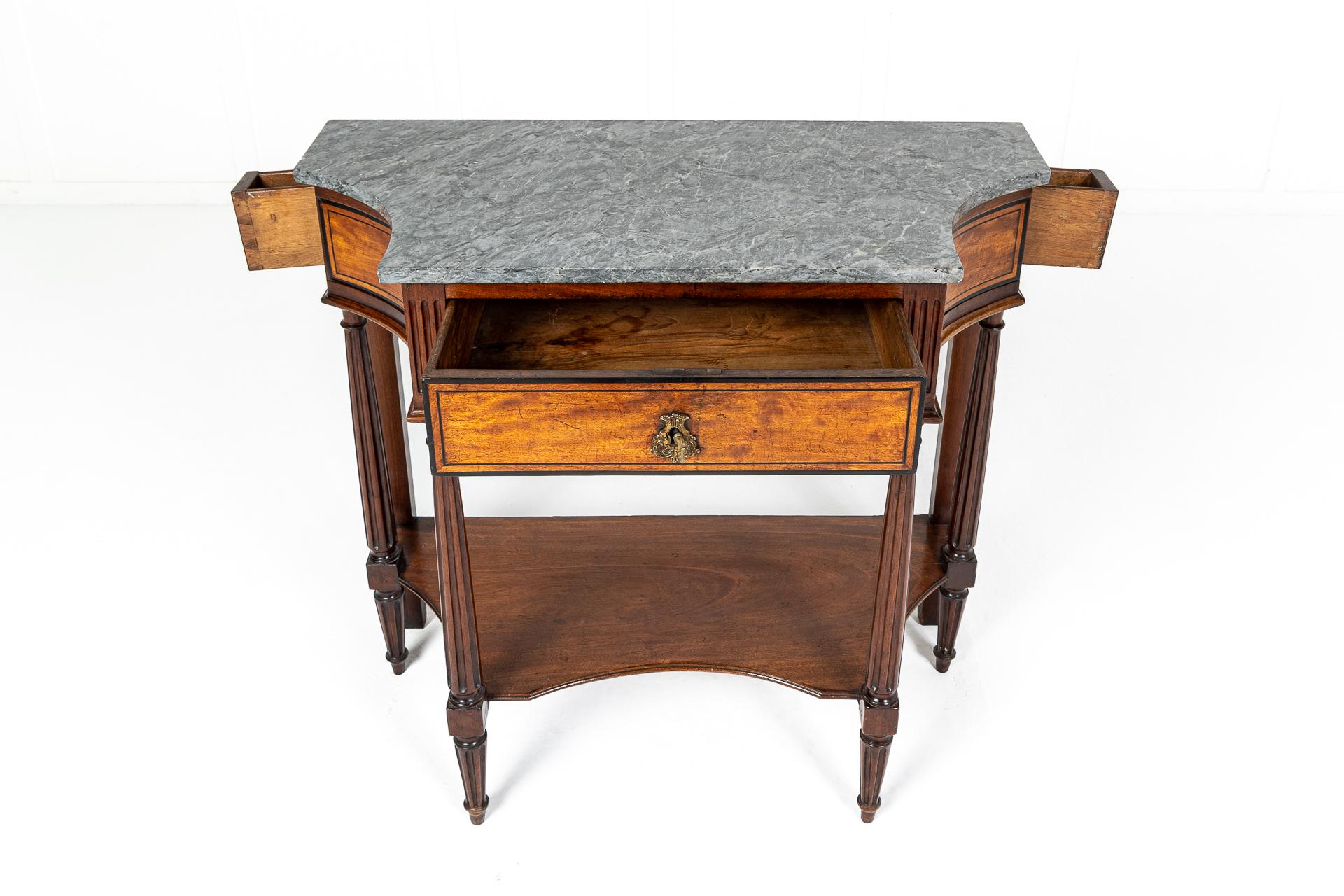 An unusual model of an early 19th century French walnut and satinwood console table having a nice original grey and white veined marble top conforming to the interesting concave sides of the table. The deep frieze has ebony inlayed drawers and