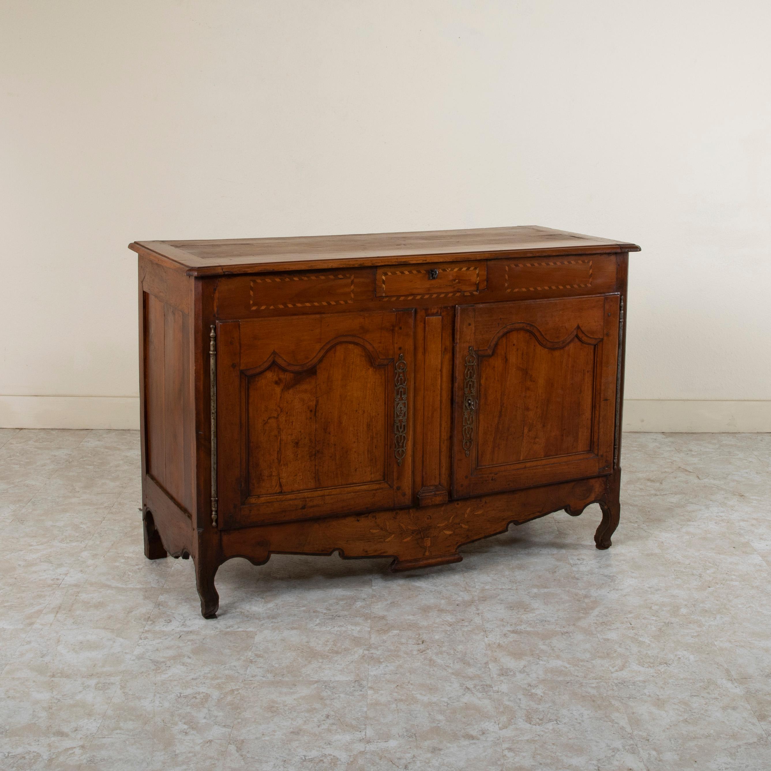 From the Dordogne region of France, this early nineteenth century walnut buffet features marquetry detailing of an urn with flowers on the lower apron and inset borders in a twisted ribbon pattern below the top. With hand pegged paneled sides, this