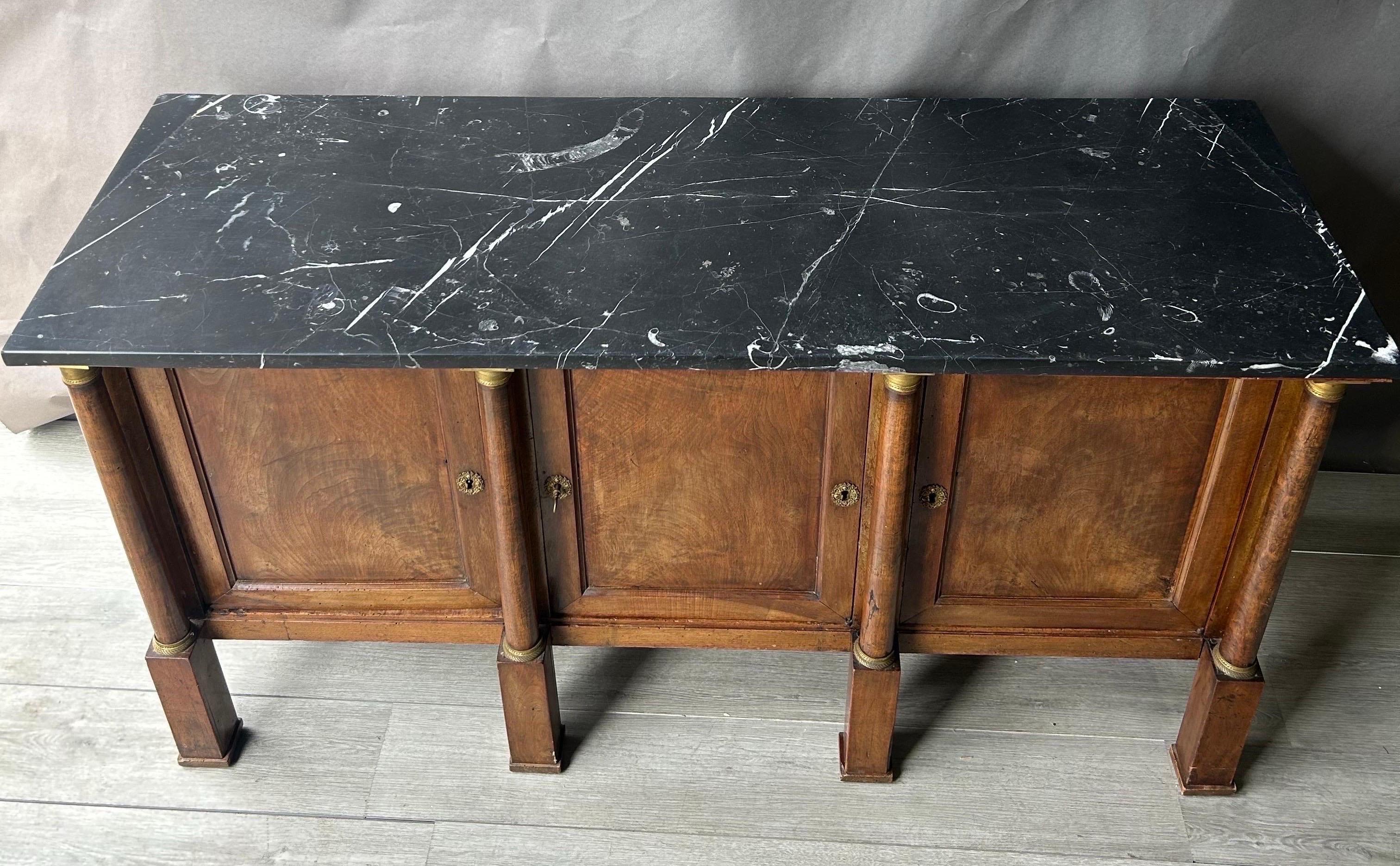 Buffet in noce Impero francese dei primi del XIX secolo con marmo fossilizzato originale. Il buffet o credenza è dotato di tre ante racchiuse da colonne montate in bronzo e si erge orgoglioso su alti piedi in stile plinto. Una forma così bella. La