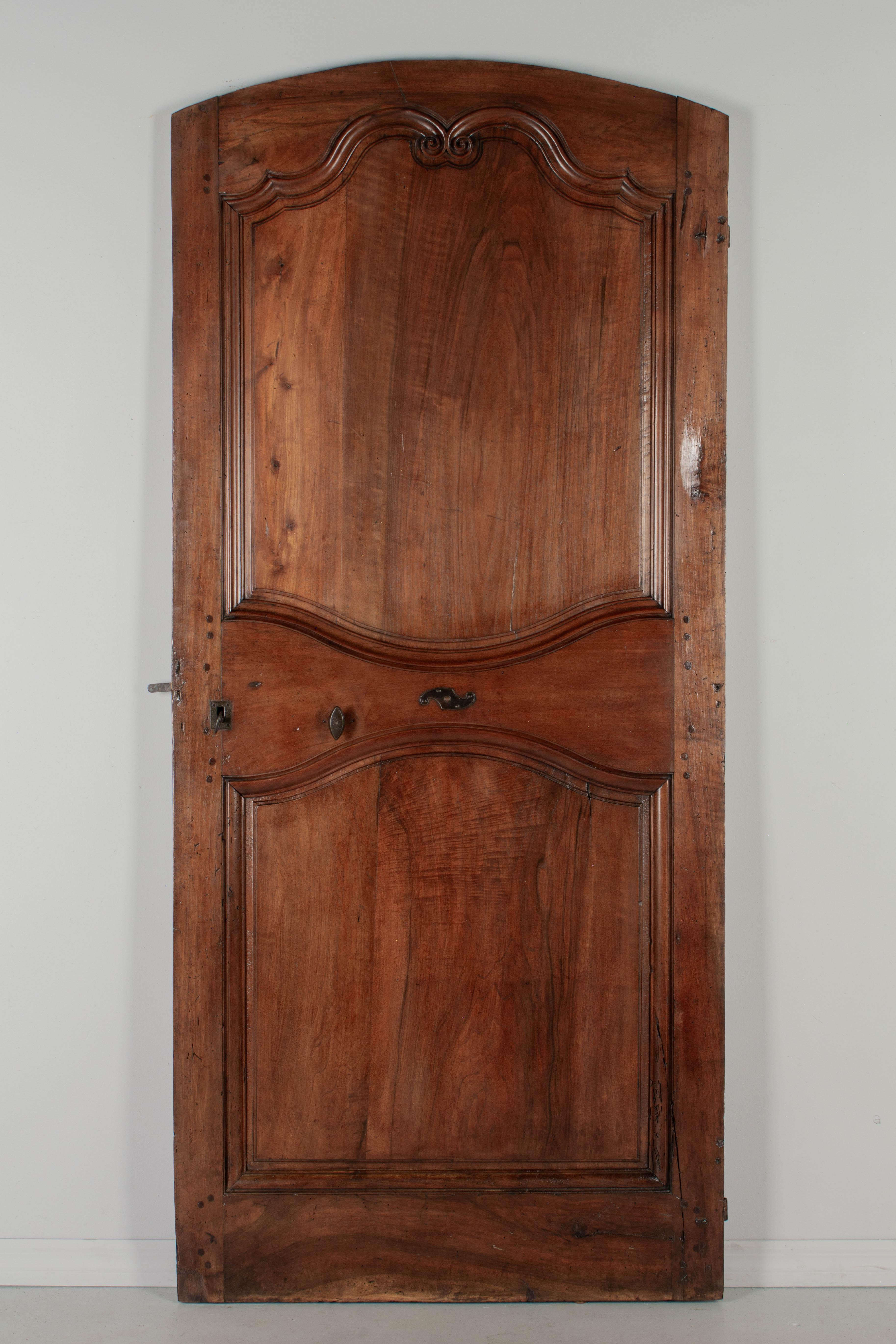 A 19th Century Louis XV style walnut door from the Loire Valley. This two sided interior door is made of thick planks of solid walnut with hand carved scroll decoration typical of the region. Large iron hinges. Working lock and key. Pegged