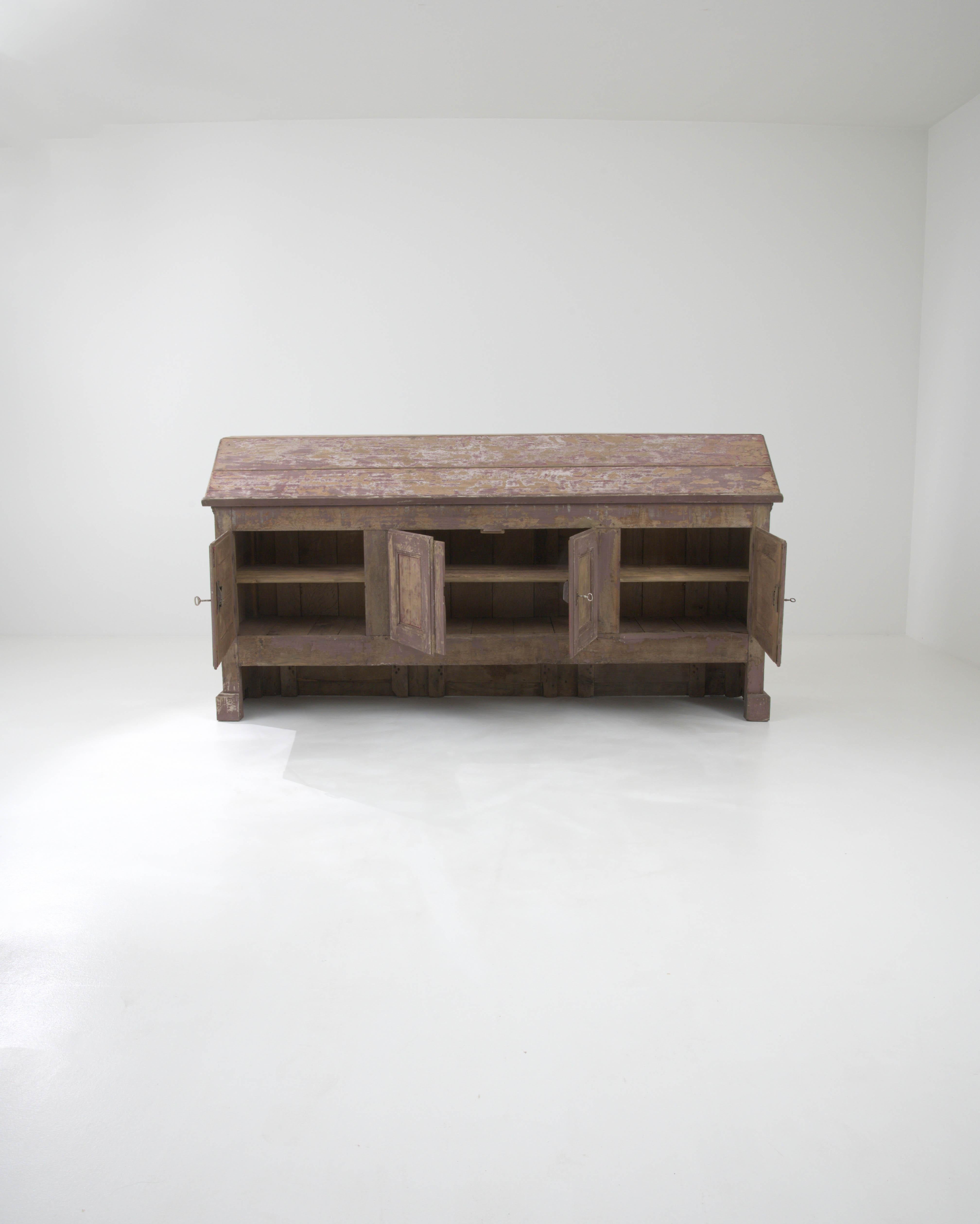 This Early 19th Century French Wood Patinated Buffet is a venerable piece that exudes the rustic elegance of provincial France. Crafted from sturdy wood, its surface wears the passage of time with a gracefully aged patina, telling tales of countless