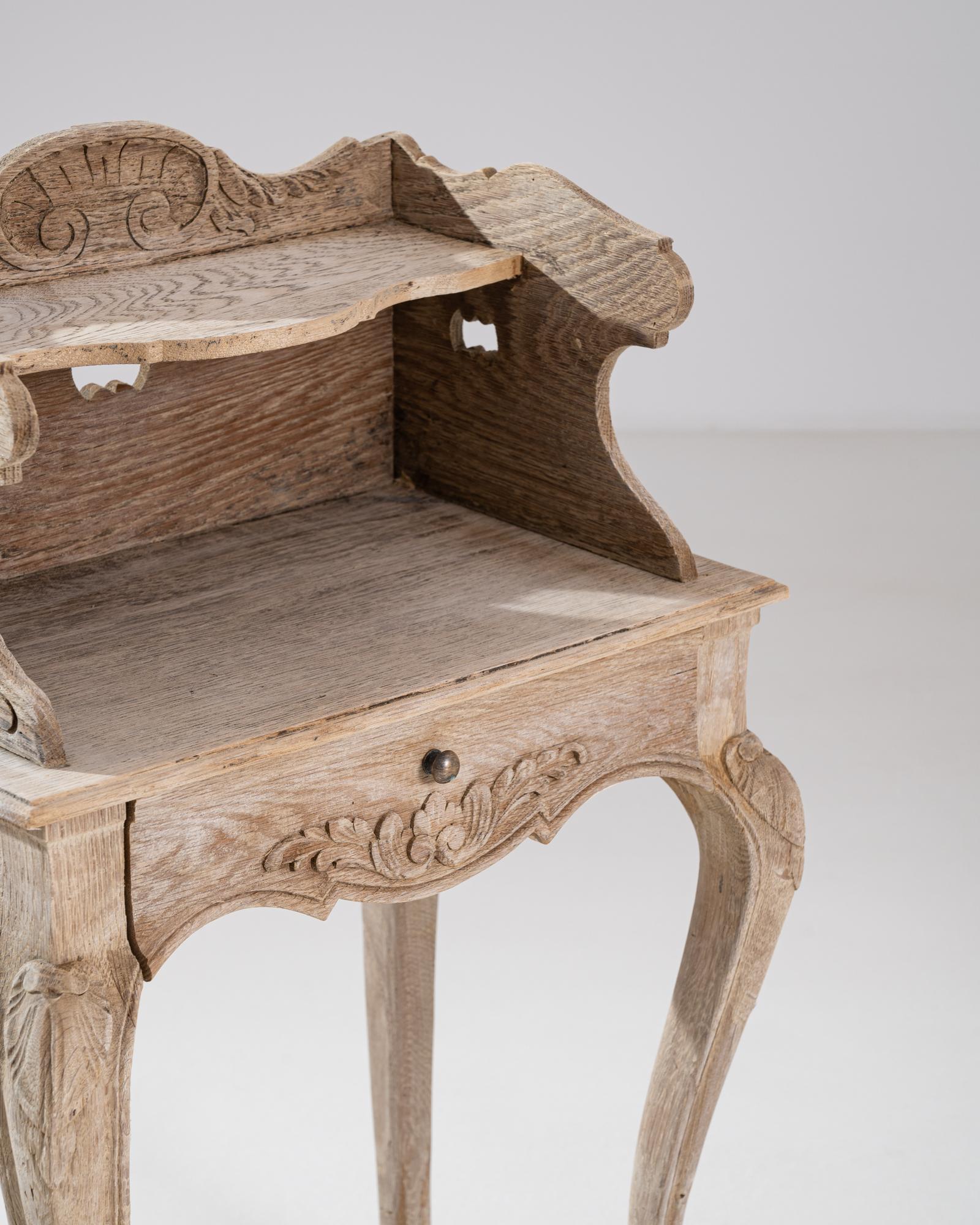 A wooden side table made in early 19th century France. This small table features a drawer and shelf with carved surround. Intricate scroll and leaf patterning eases the eye on each side of this unique table, and artfully sloping legs buttress it.