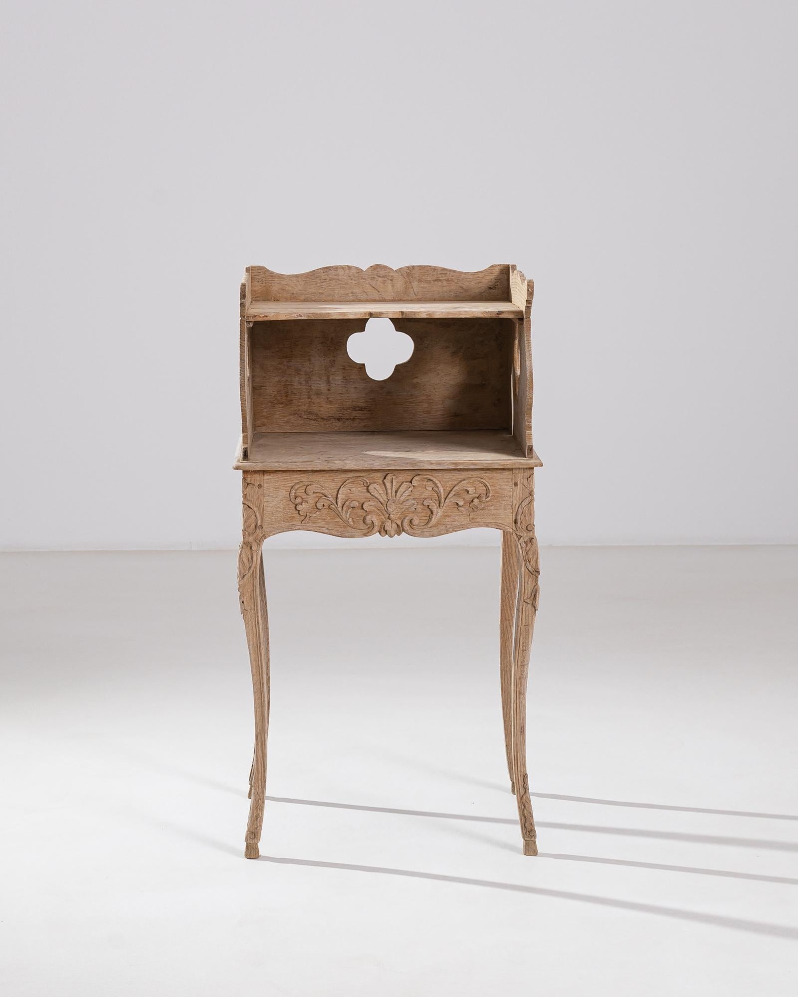 A wooden side table made in early 19th century France. This small table features a drawer and shelf with carved surround. Intricate scroll and leaf patterning eases the eye on each side of this unique table, and artfully sloping legs buttress it.