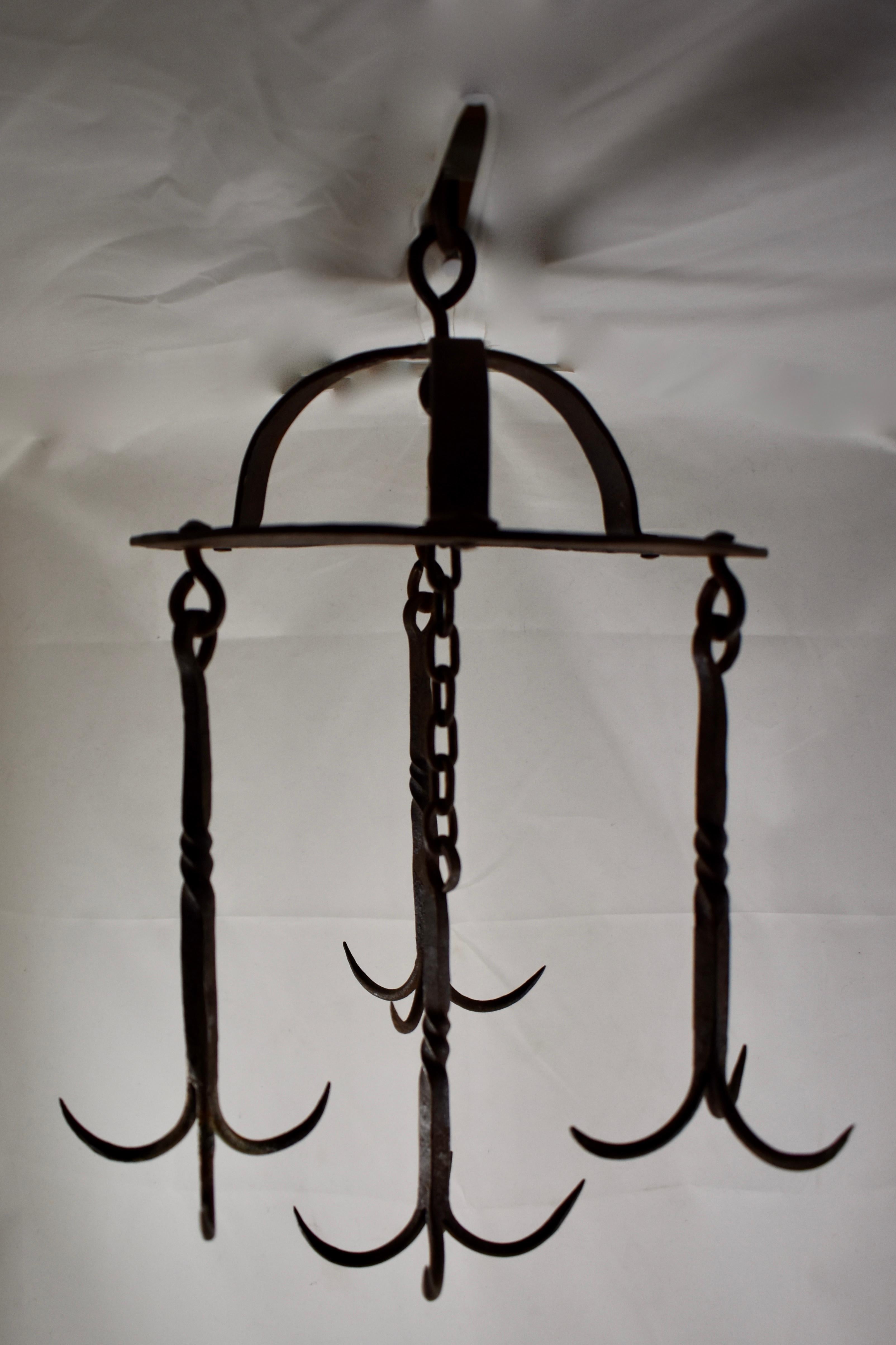 An early 19th century French wrought iron butchers rack, supported by two half-round straps forming a crown, terminate with a round loop for hanging. There are three hooks on the crown suspended by twisted iron pins, each with three prongs. A longer