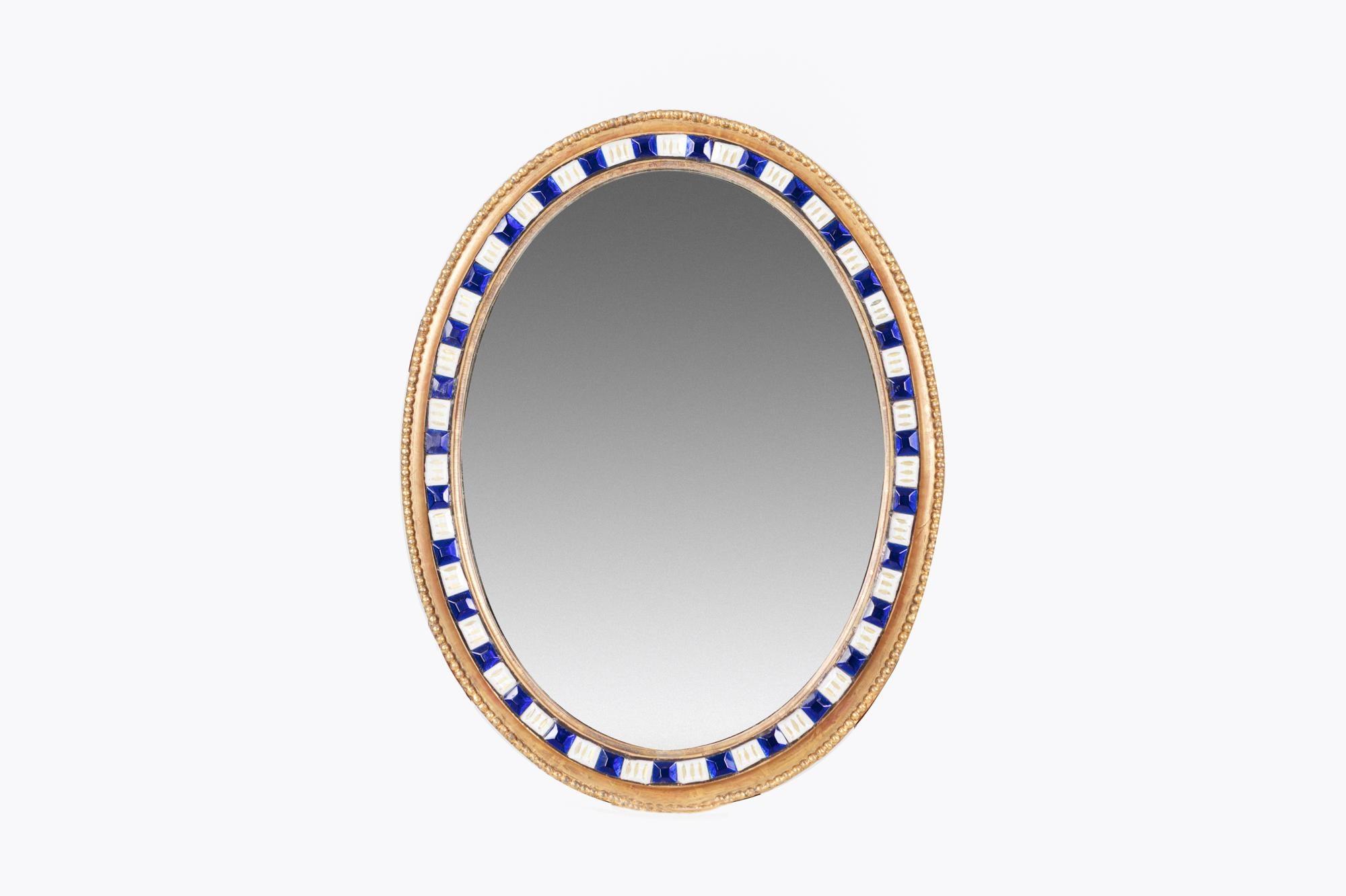 Early 19th century Irish George III Waterford large wall mirror of oval form, the giltwood frame with carved gadrooned edge and beading detail encompassing alternating faceted blue and white glass studs, circa 1800.