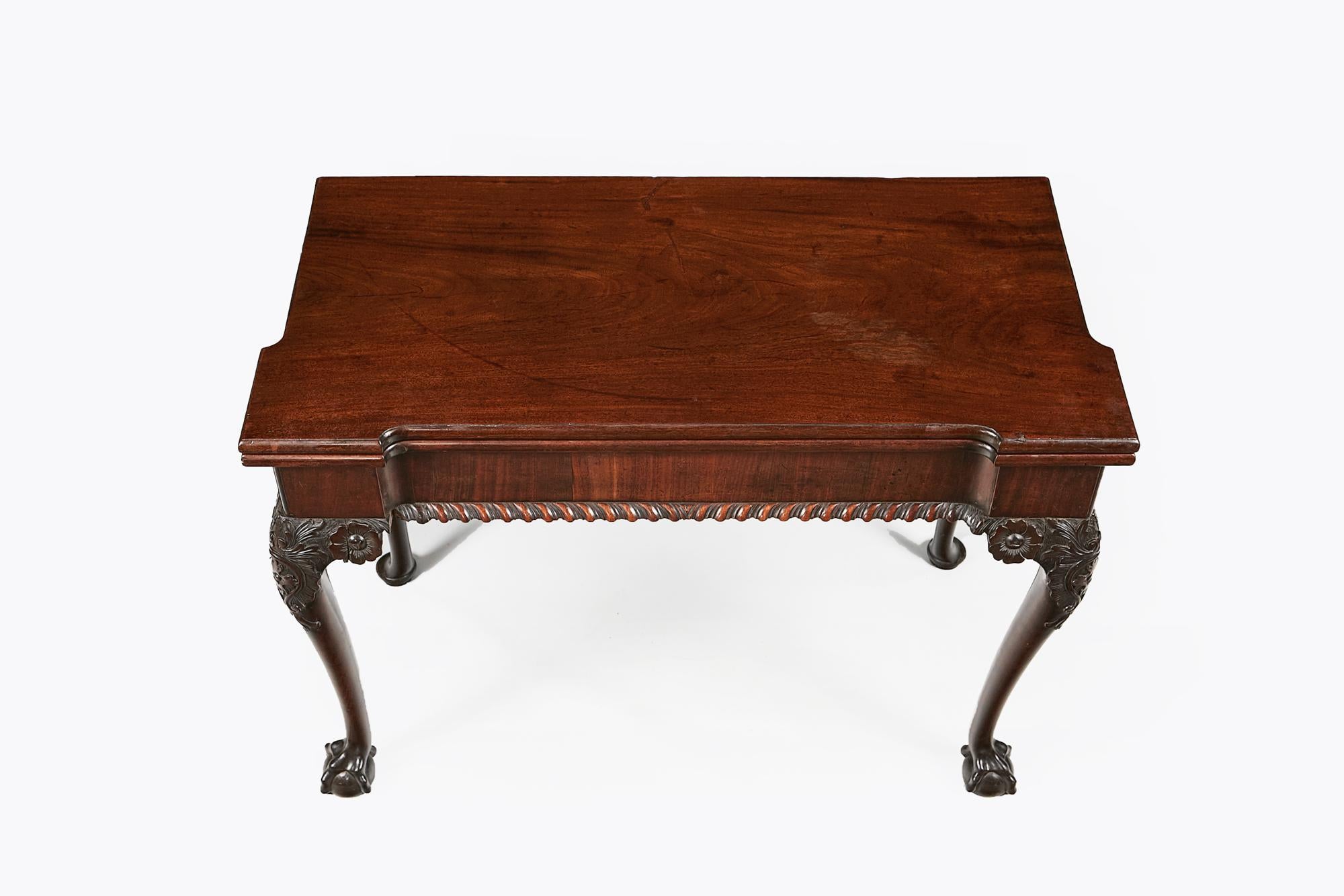 Early 19th century George III mahogany fold-over card table, the shaped and moulded top raised over frieze with carved gadroon motif supported on cabriole leg with foliate motif on knee terminating on ball and claw foot.