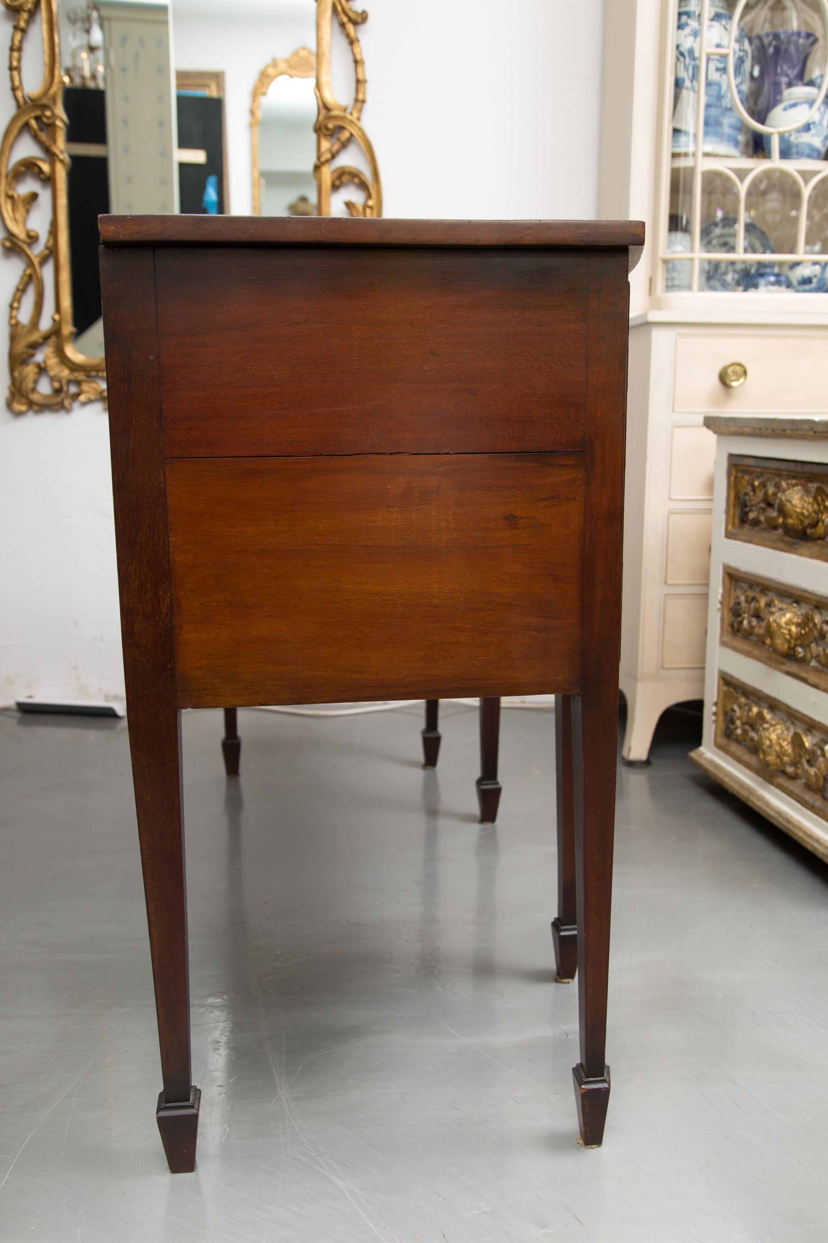 This is a Classic English George III mahogany bow front sideboard. The top with straight edge is over a conforming case containing a central drawer flanked by a pair of cabinet doors. The case piece is supported by straight tapered legs terminating